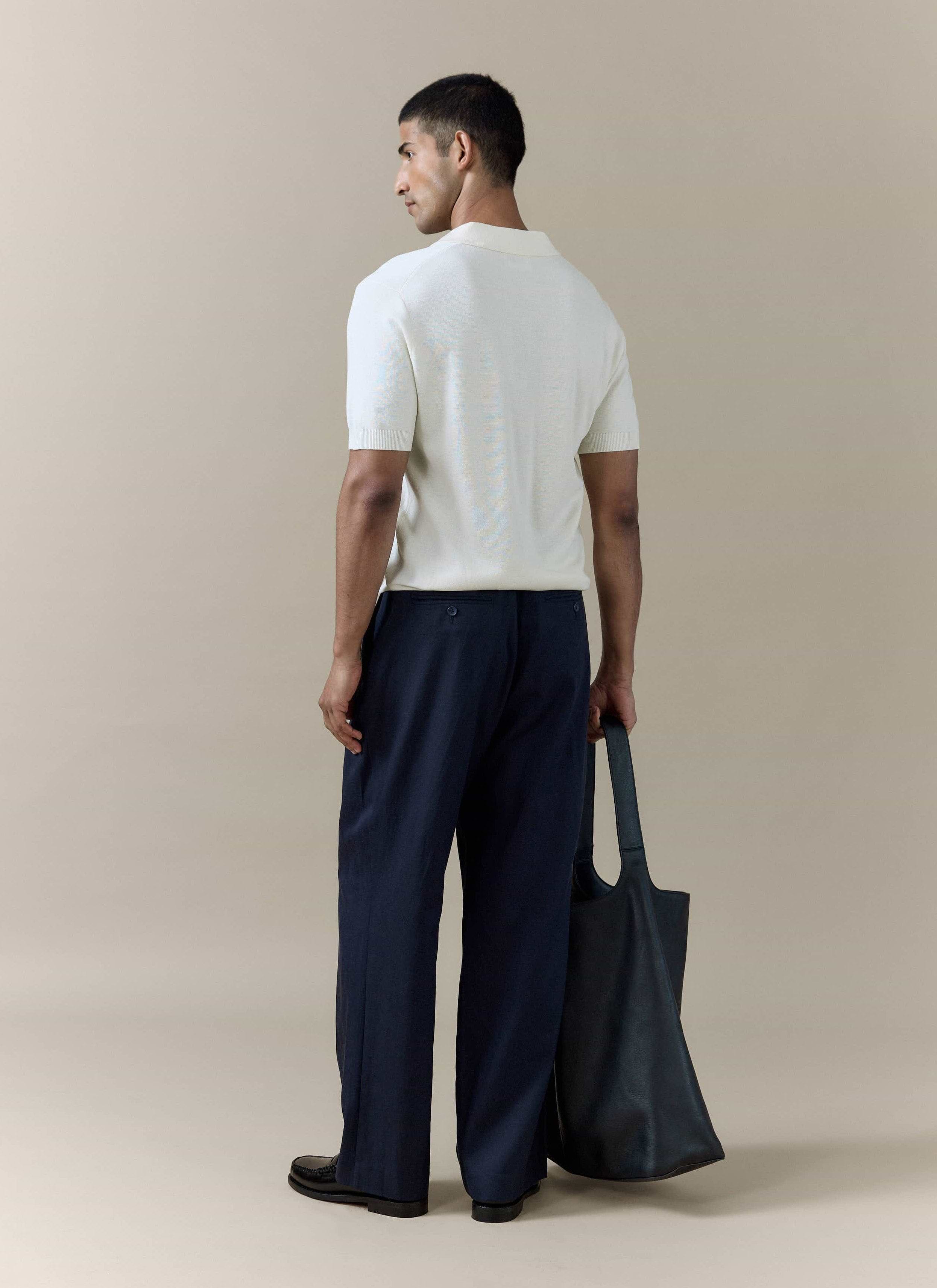Rear view of the cream Laurence Knitted Polo by Percival in a linen blend, styled with navy trousers and a black tote.