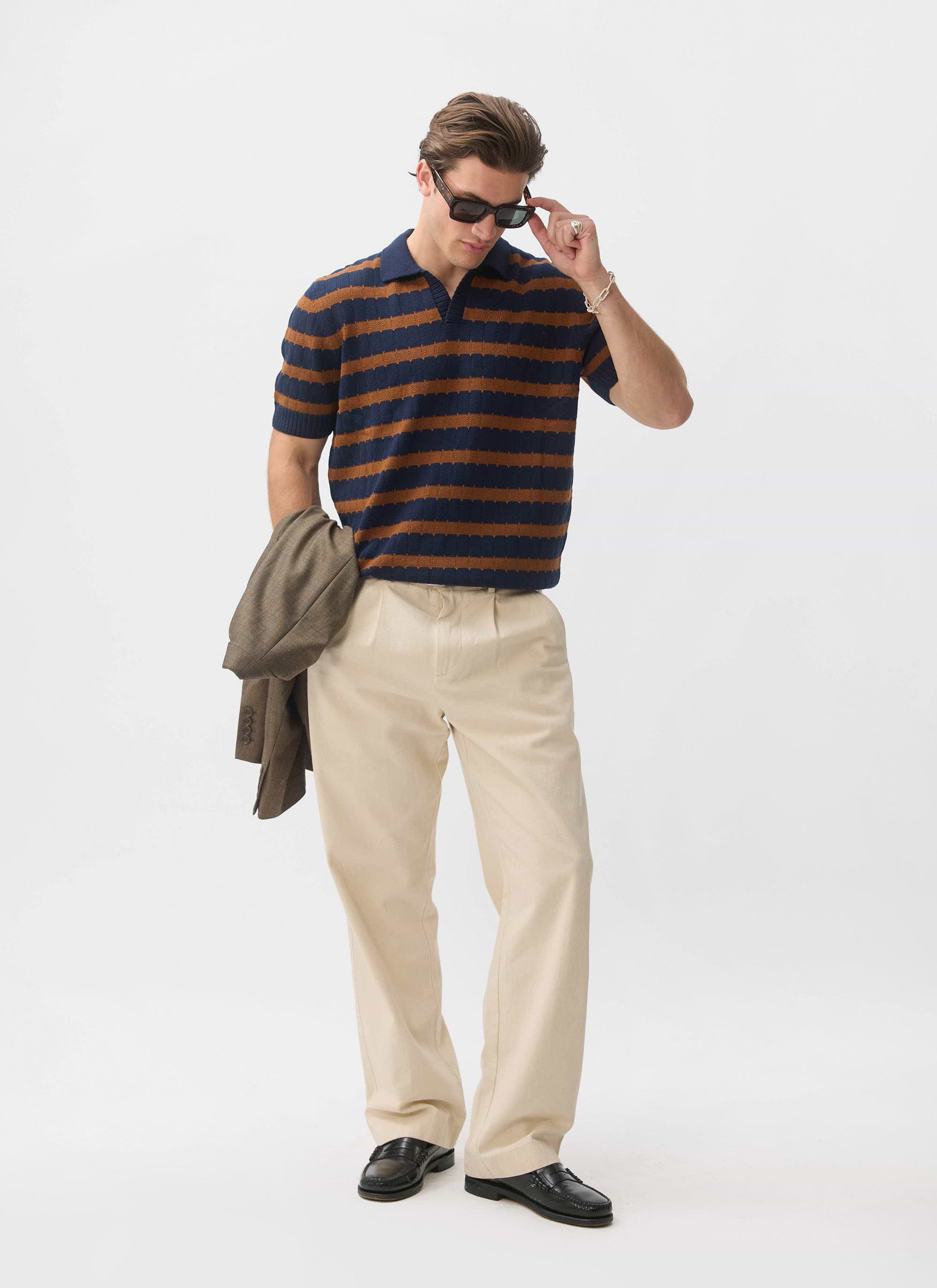 A model wears the Percival Stine Knitted Polo in brown and navy stripes, styled with beige trousers and sunglasses.