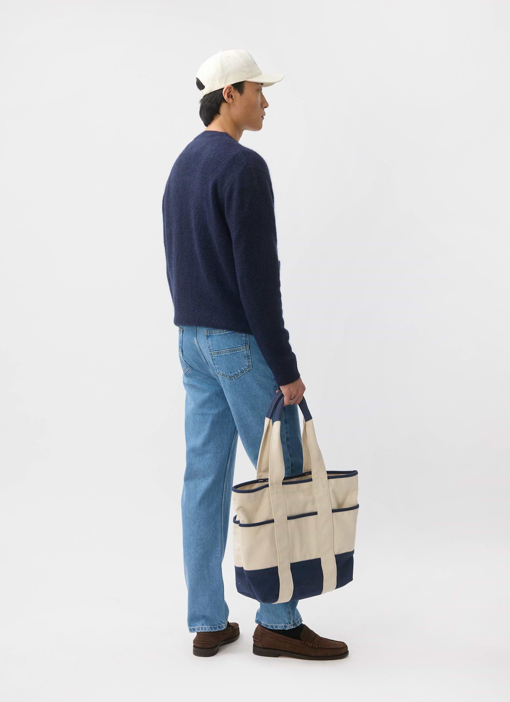 A model, seen from the side, wears the Percival White Glove mohair cardigan in navy with blue jeans and a white cap.