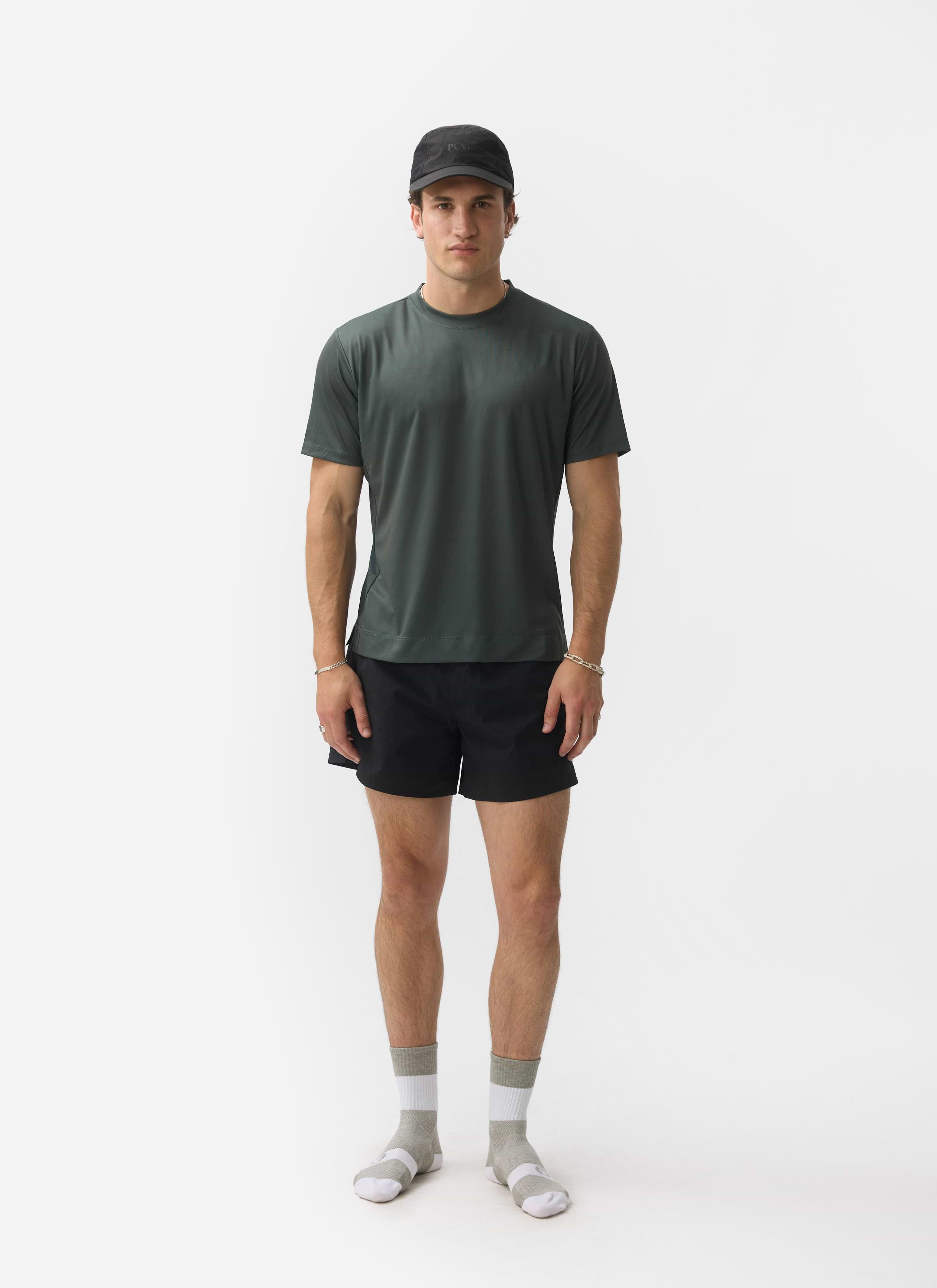 A model wears the Percival PCVL Performance Top in Forest green with black shorts and a cap against a white background.