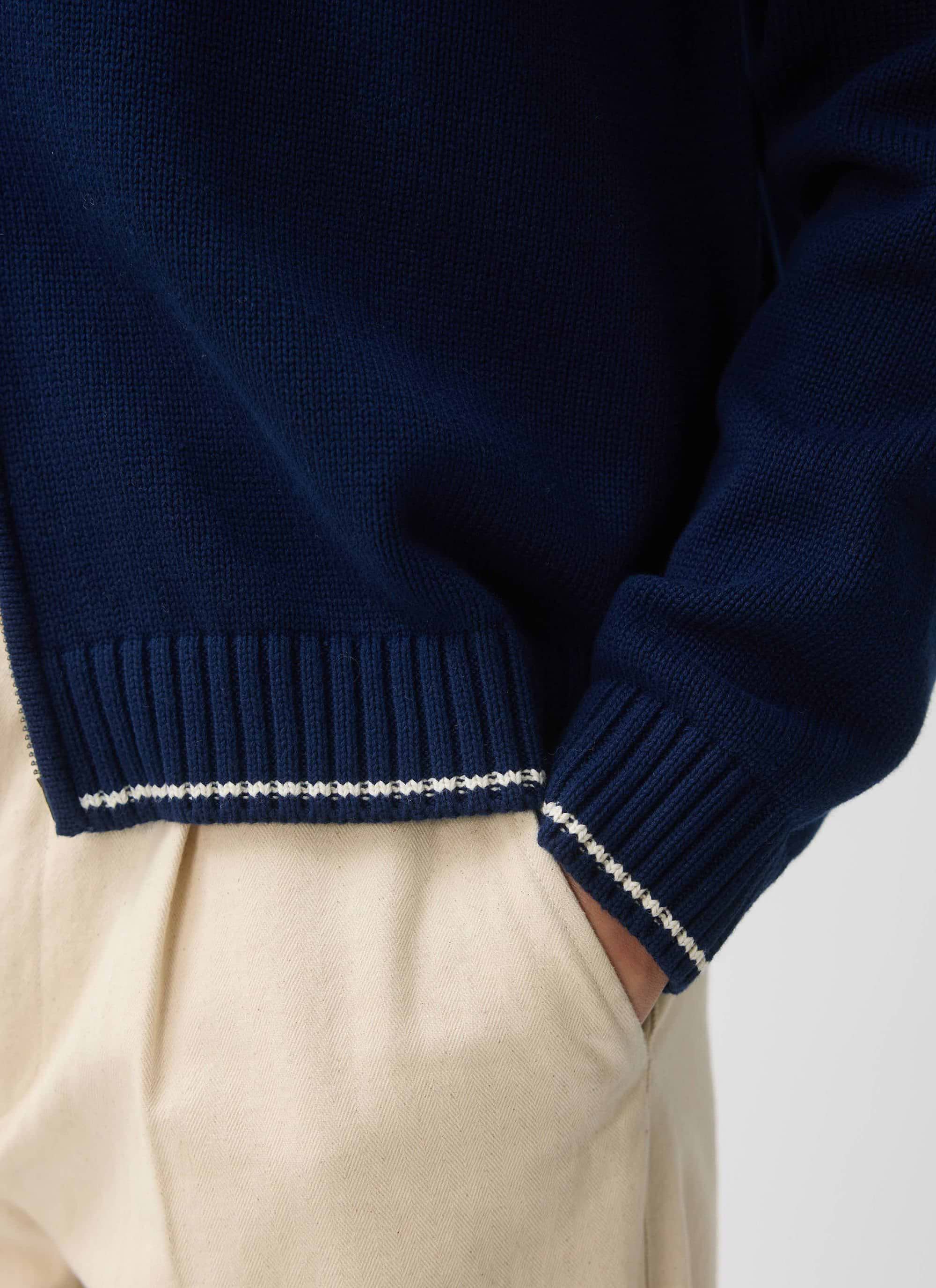A close-up of the ribbed hem on the Percival Gardner Dense Knitted Zip Cardigan in navy, showing the white stitch detail.