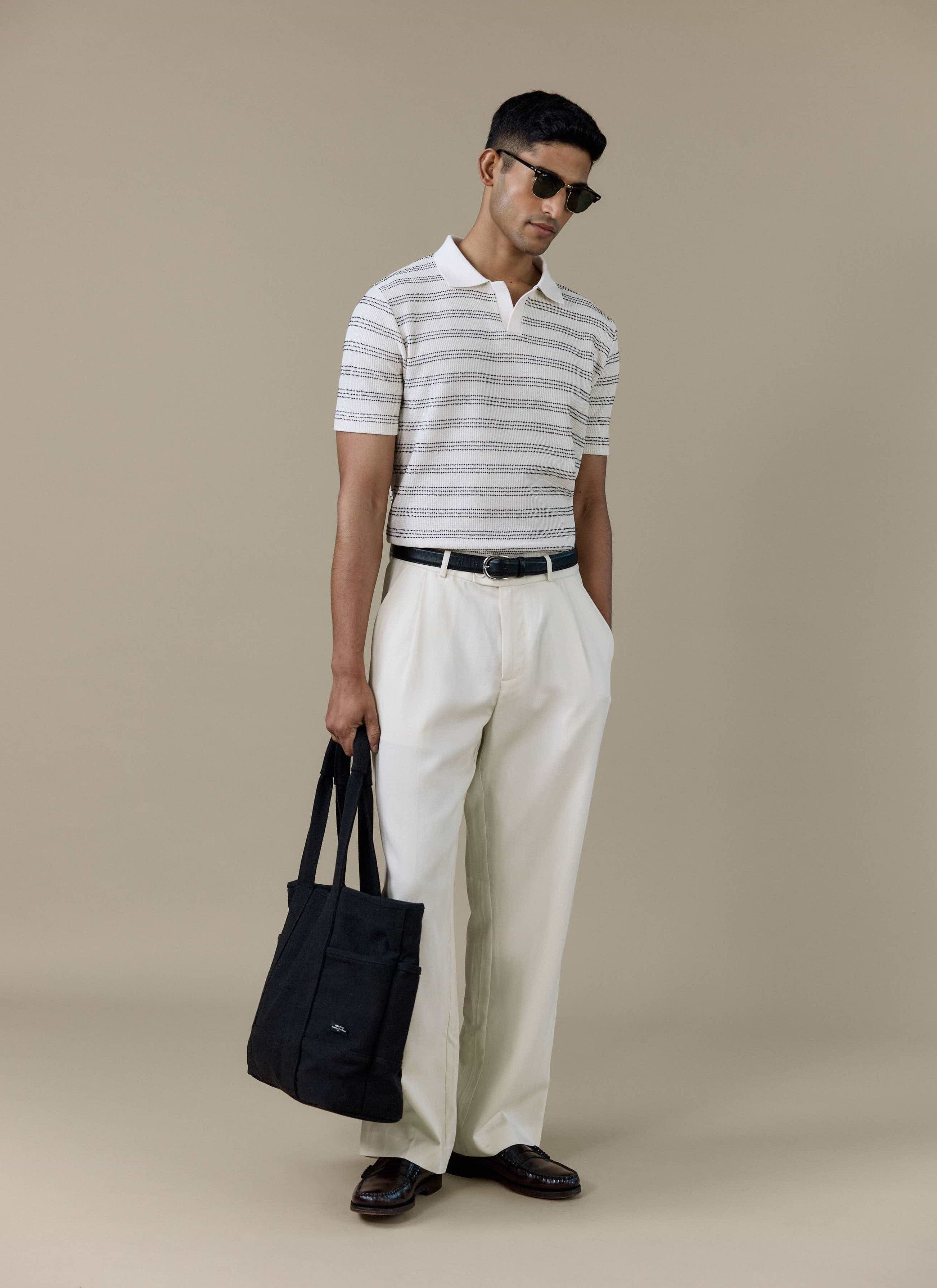 A model wearing the Percival Laurent Boxy Polo in cream stripe, styled with cream trousers and a black tote bag.