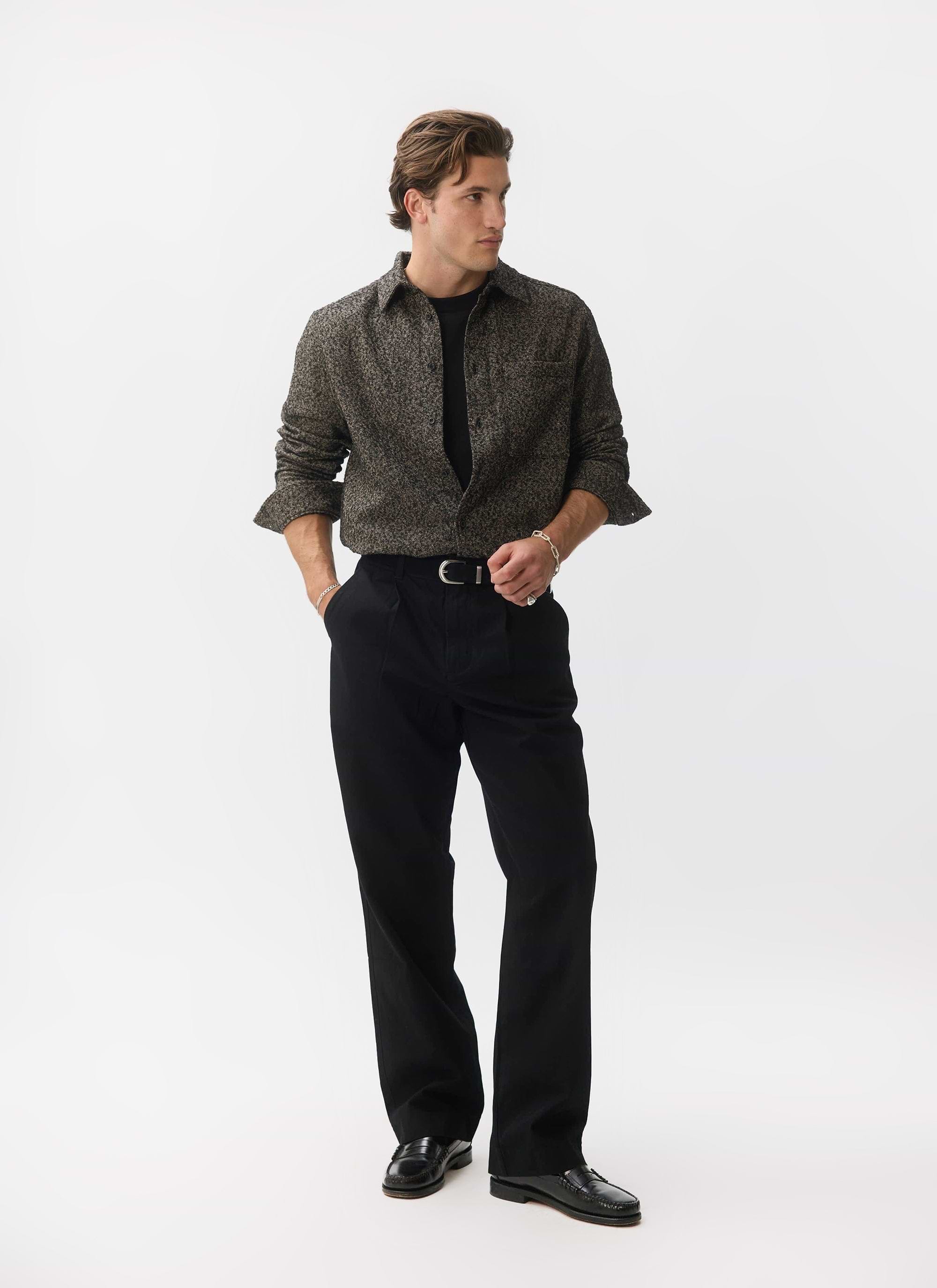 A man models the Percival Blyton Long Sleeve Shirt in grey, styled over a black t-shirt with smart black trousers.