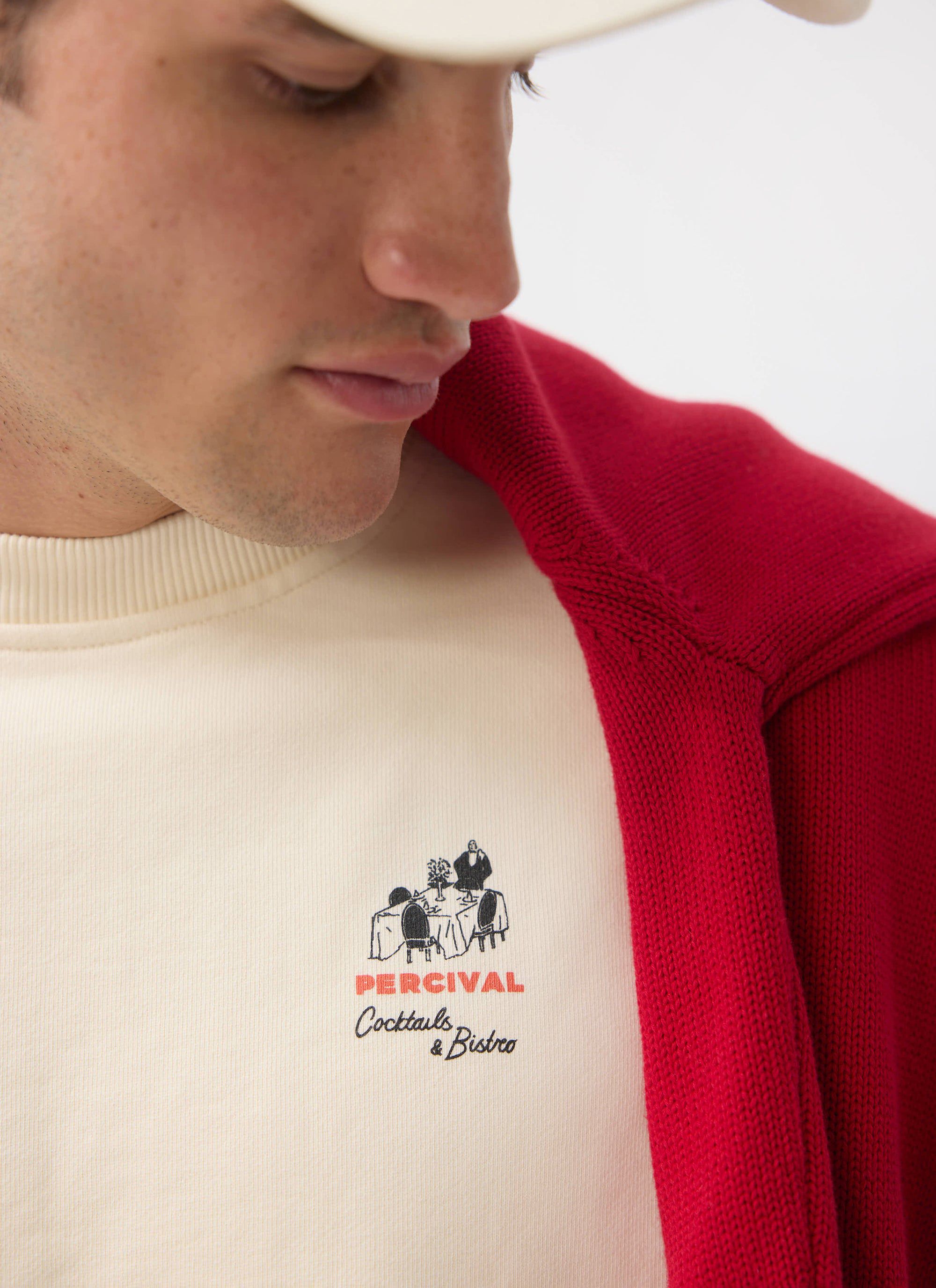 A model wears the ecru Bistro sweatshirt from Percival, in a close-up shot focusing on the chest embroidery.