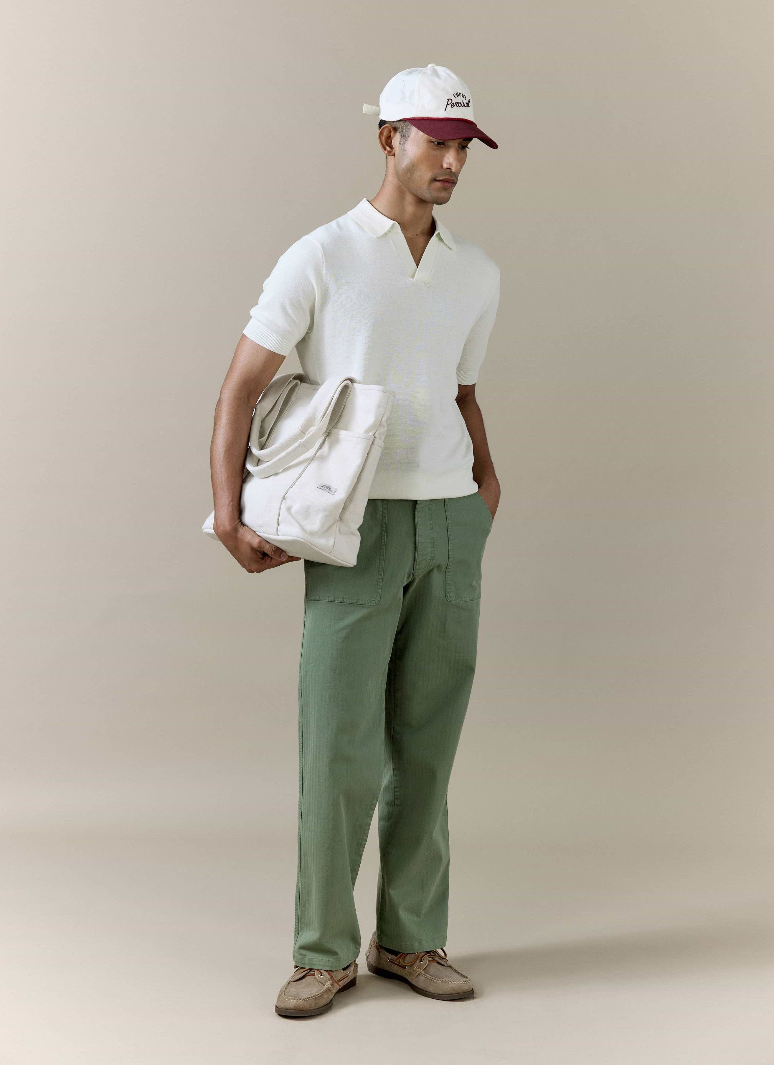 Cream linen-blend Laurence Knitted Polo by Percival, styled with an open Johnny collar, green trousers and a tote bag.