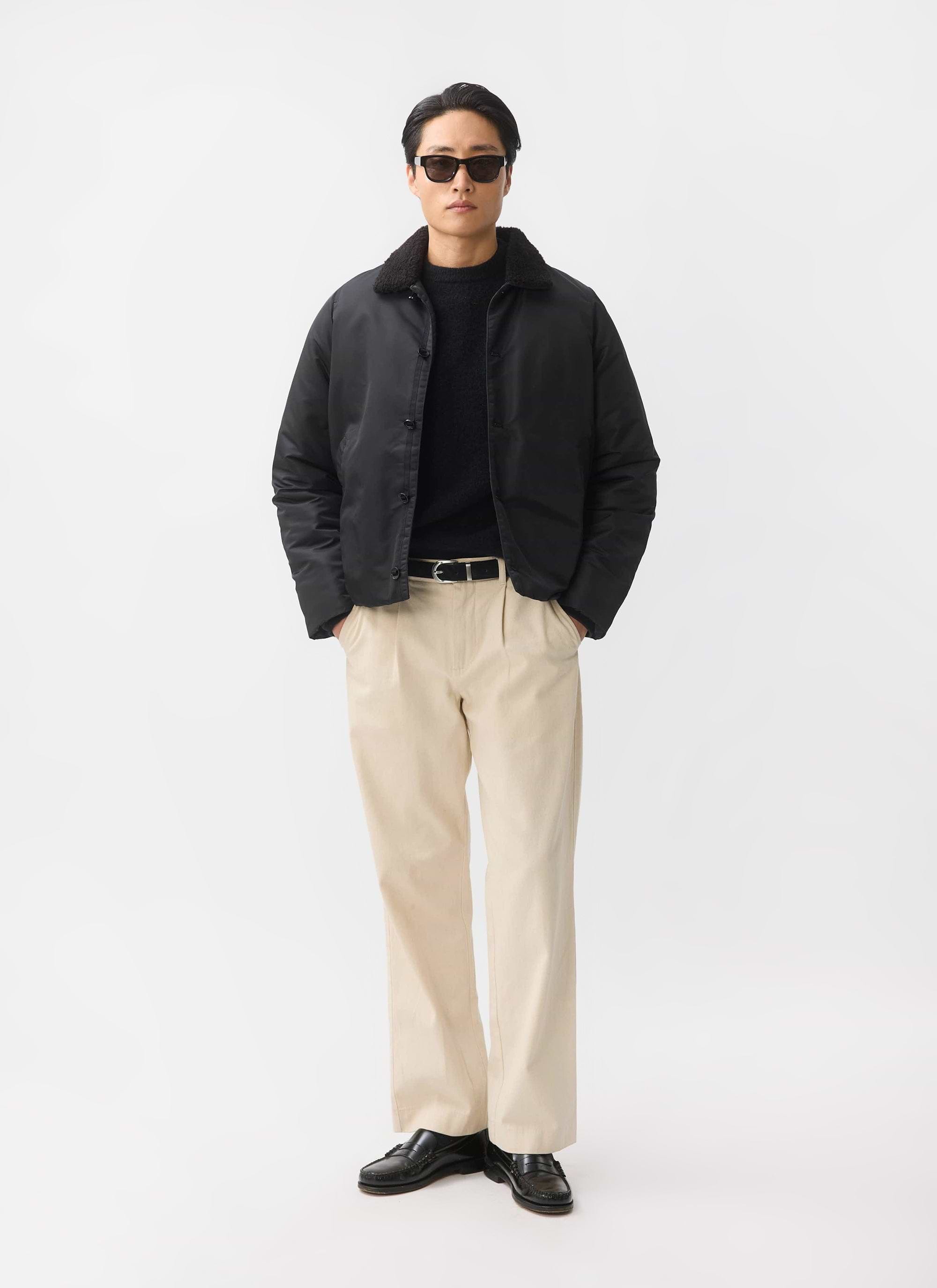 A model styles the black Doppio Bomber Jacket from Percival with a shearling collar, sunglasses and beige trousers.