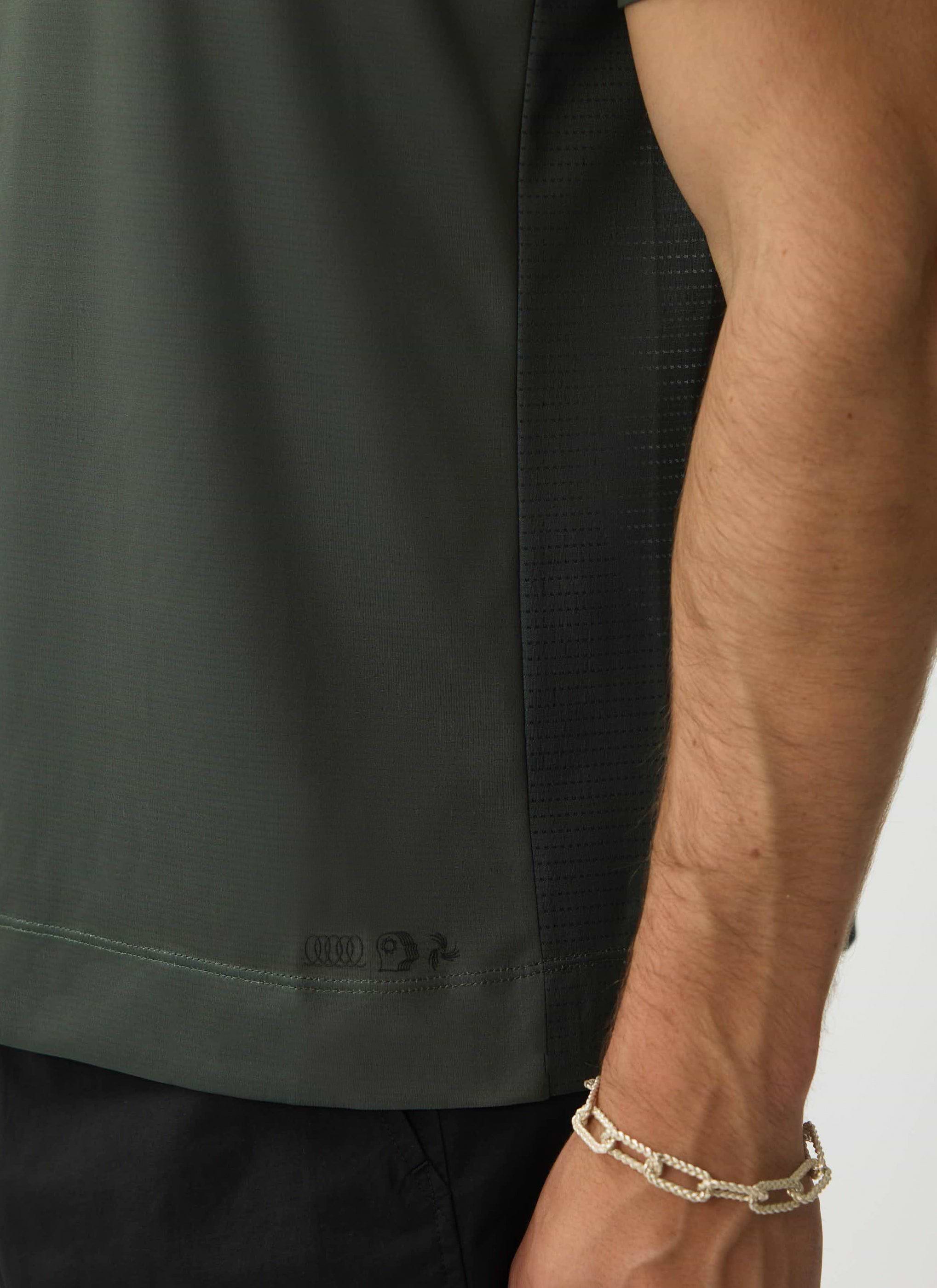 A close-up of the tonal logo embroidery and ventilated mesh panel on the Percival PCVL Performance Top in forest green.