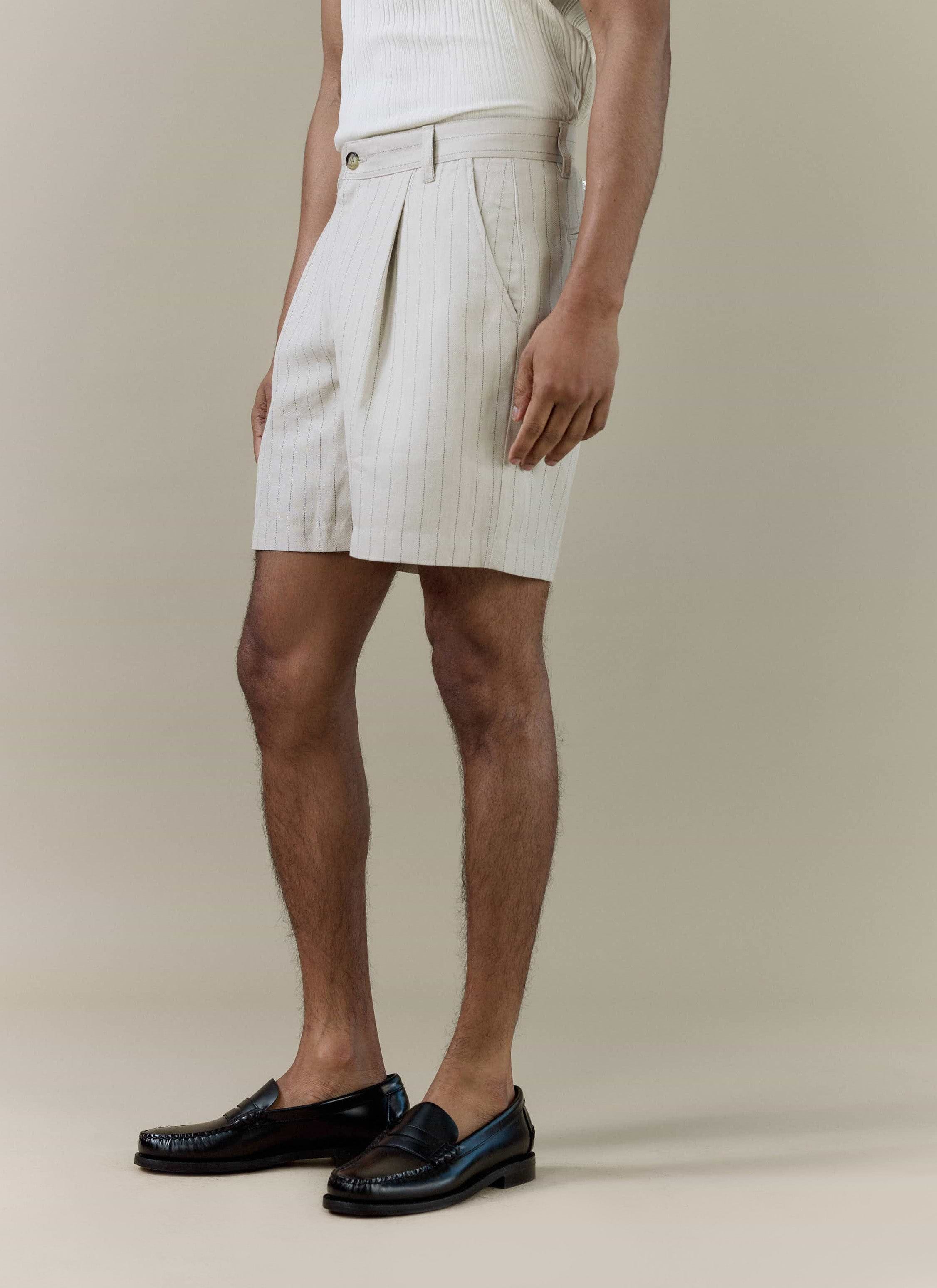 A model wears Percival pleated tailored shorts in cream striped linen blend, paired with black leather loafers.