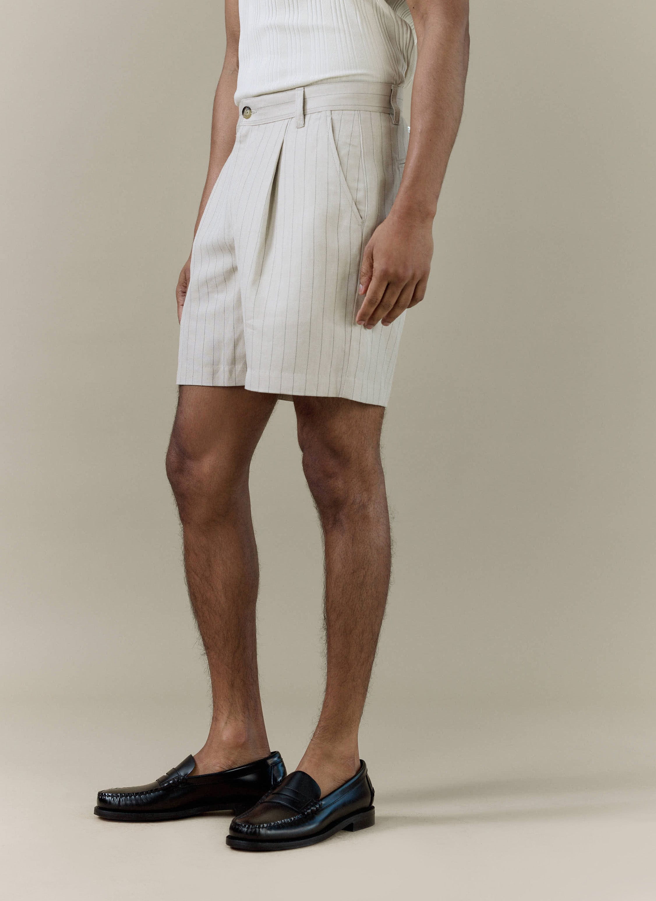A model wears Percival pleated tailored shorts in cream striped linen blend, paired with black leather loafers.