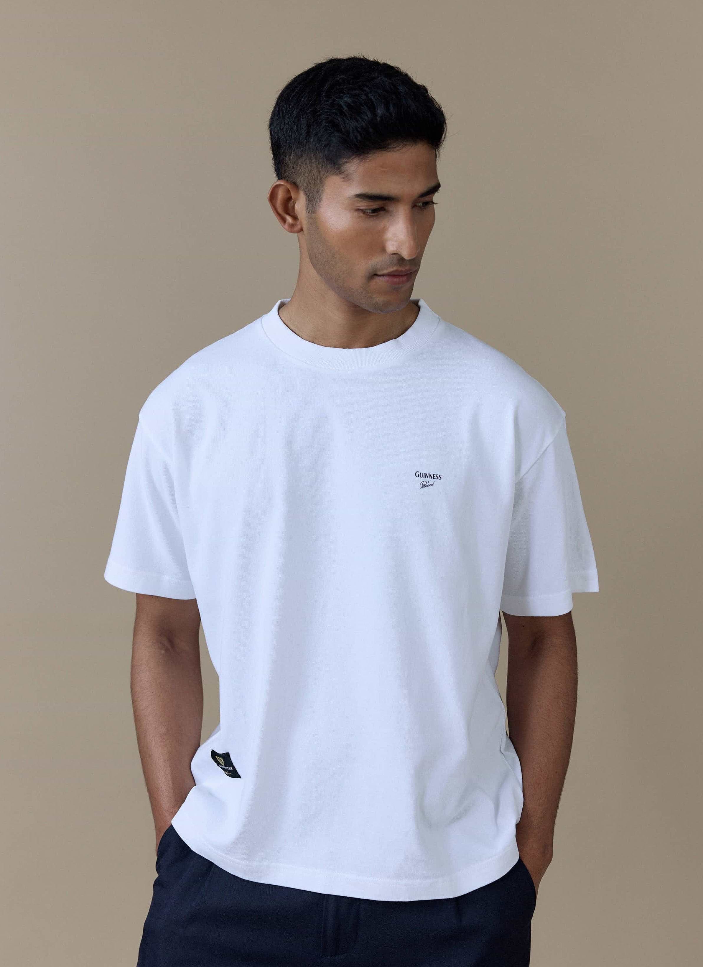 Model wearing the white Guinness x Percival Printed Oversized T-Shirt, featuring the chest logo and woven label.
