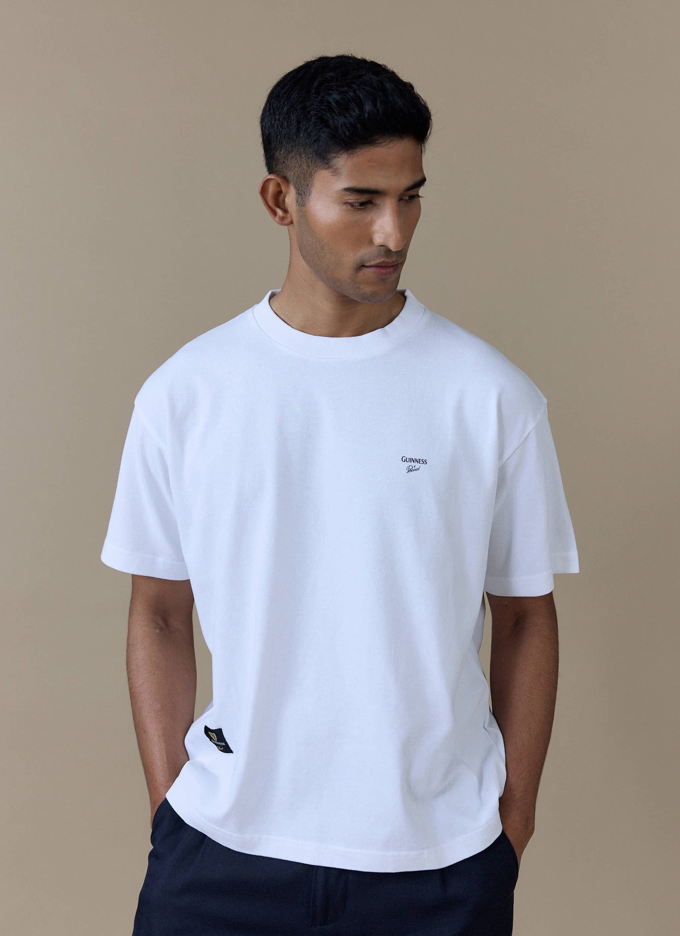 Model wearing the white Guinness x Percival Printed Oversized T-Shirt, featuring the chest logo and woven label.