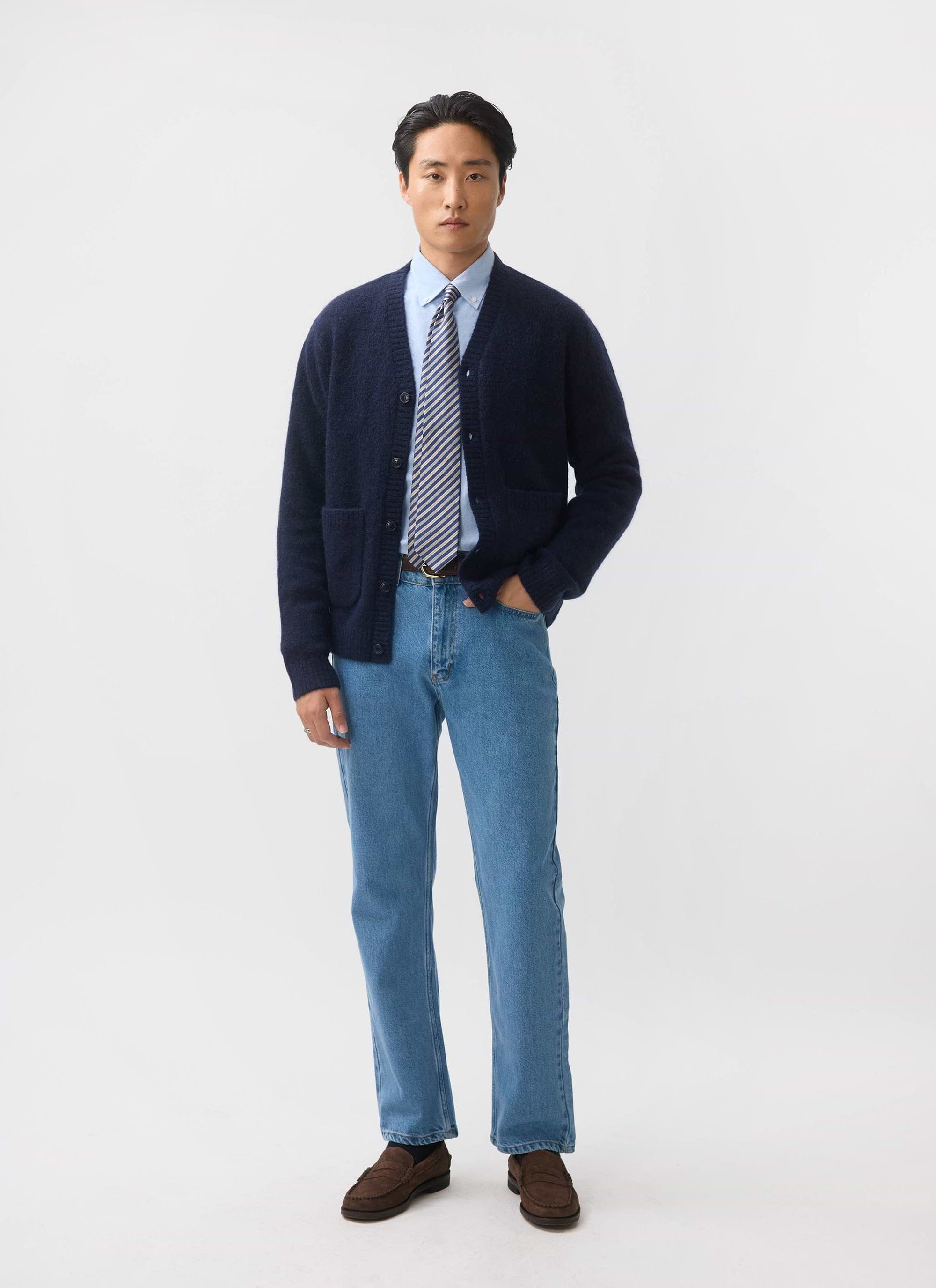 A model wears the navy mohair White Glove Cardigan from Percival, styled with a shirt, tie, and blue jeans.