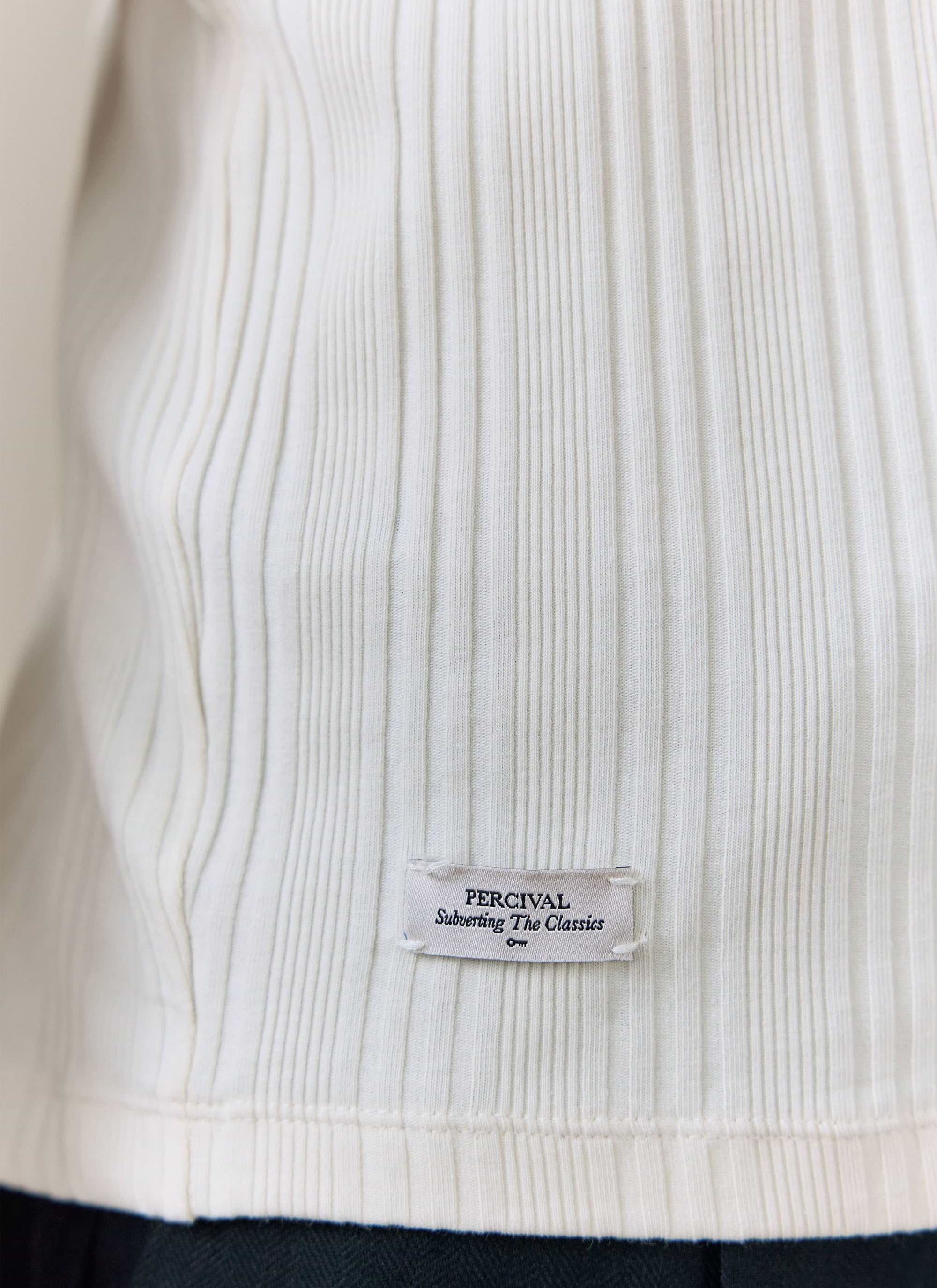 Close-up of the cream ribbed cotton Leon T-shirt by Percival, highlighting the branded 'Subverting The Classics' hem tag.