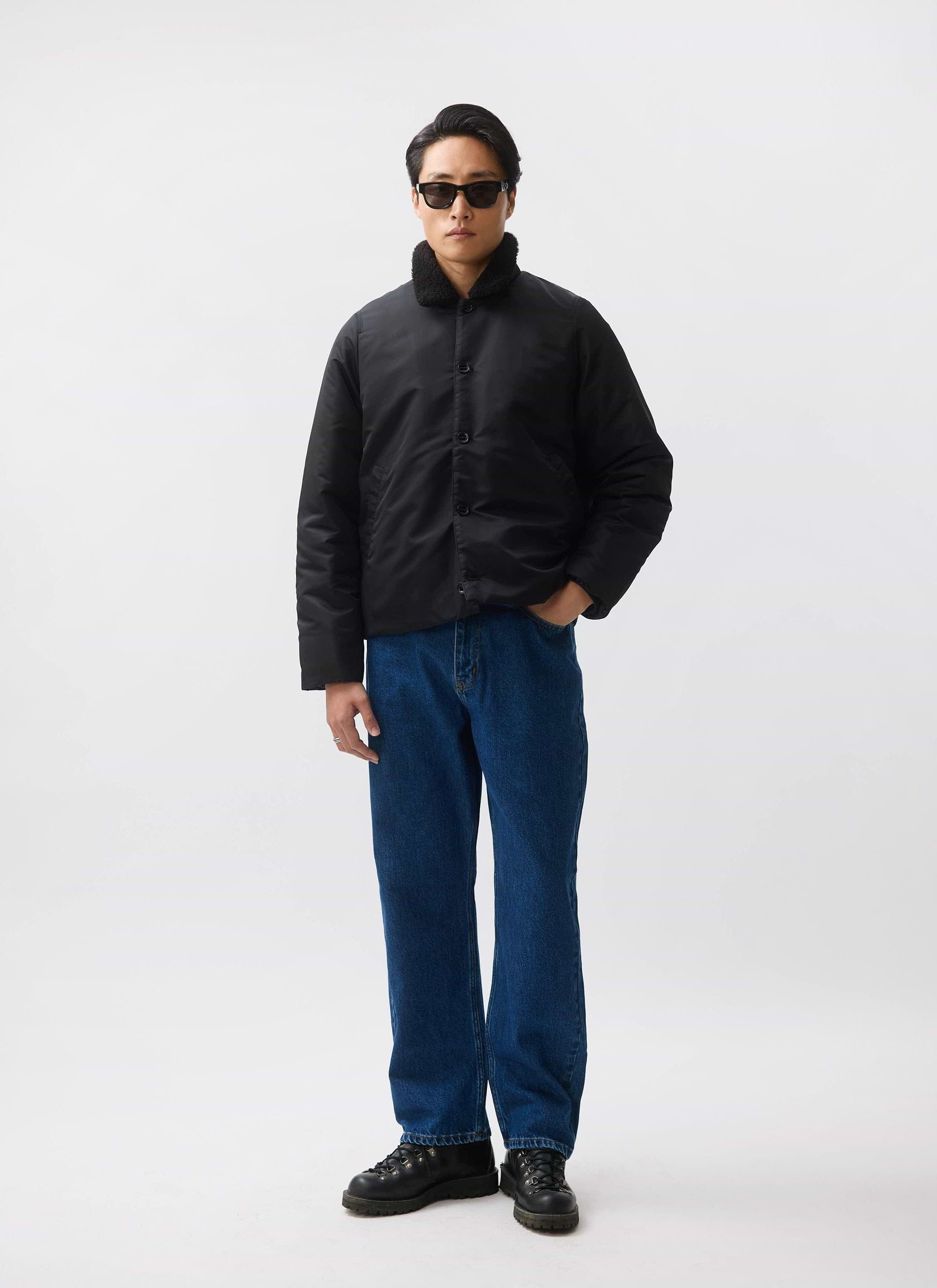 A model wears the black nylon Doppio Bomber Jacket from Percival, featuring a faux shearling collar, styled with blue jeans.