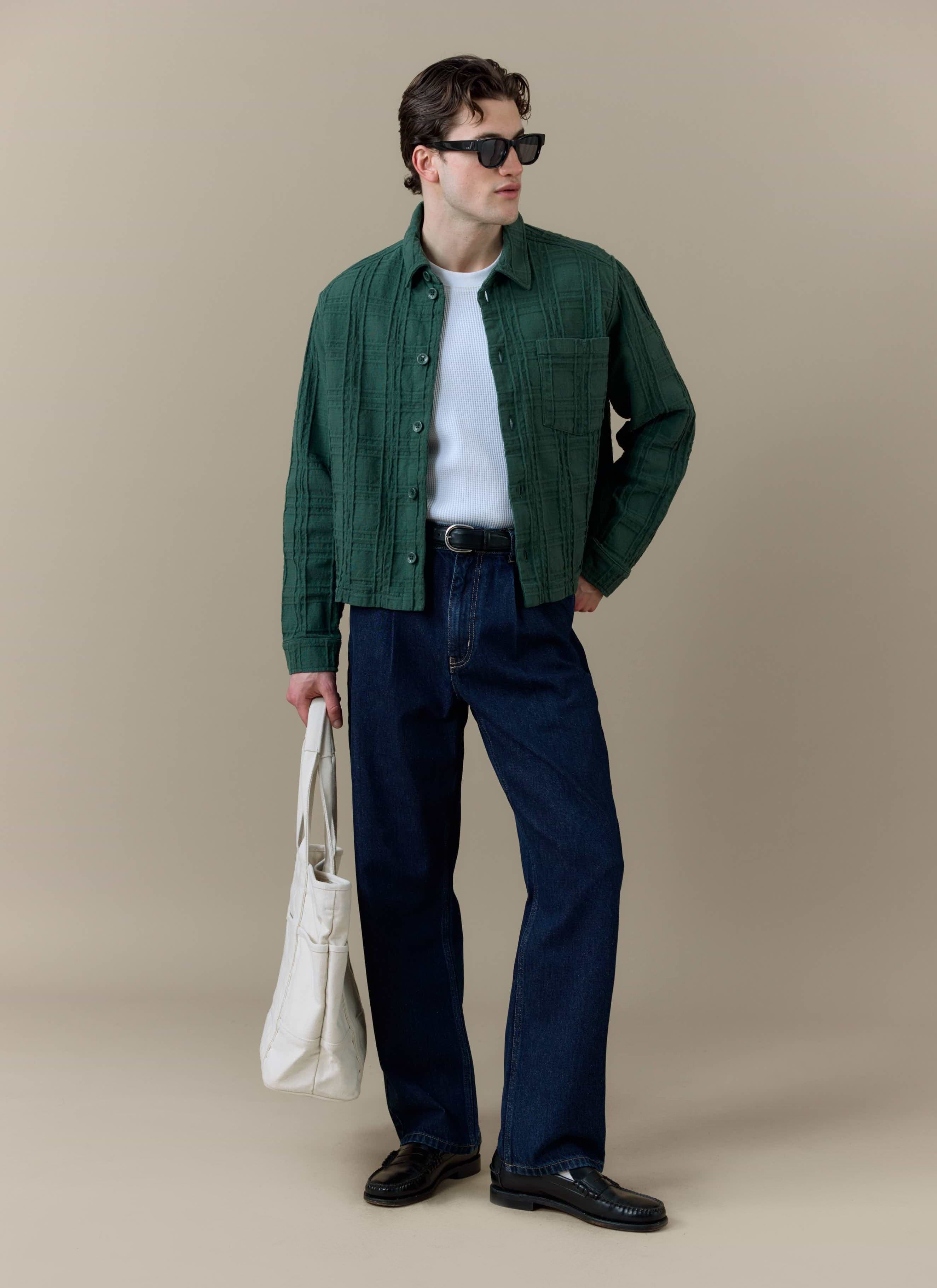 A model wearing the Percival Canyon Heavyweight Overshirt in forest green, styled with dark trousers and a white tote bag.