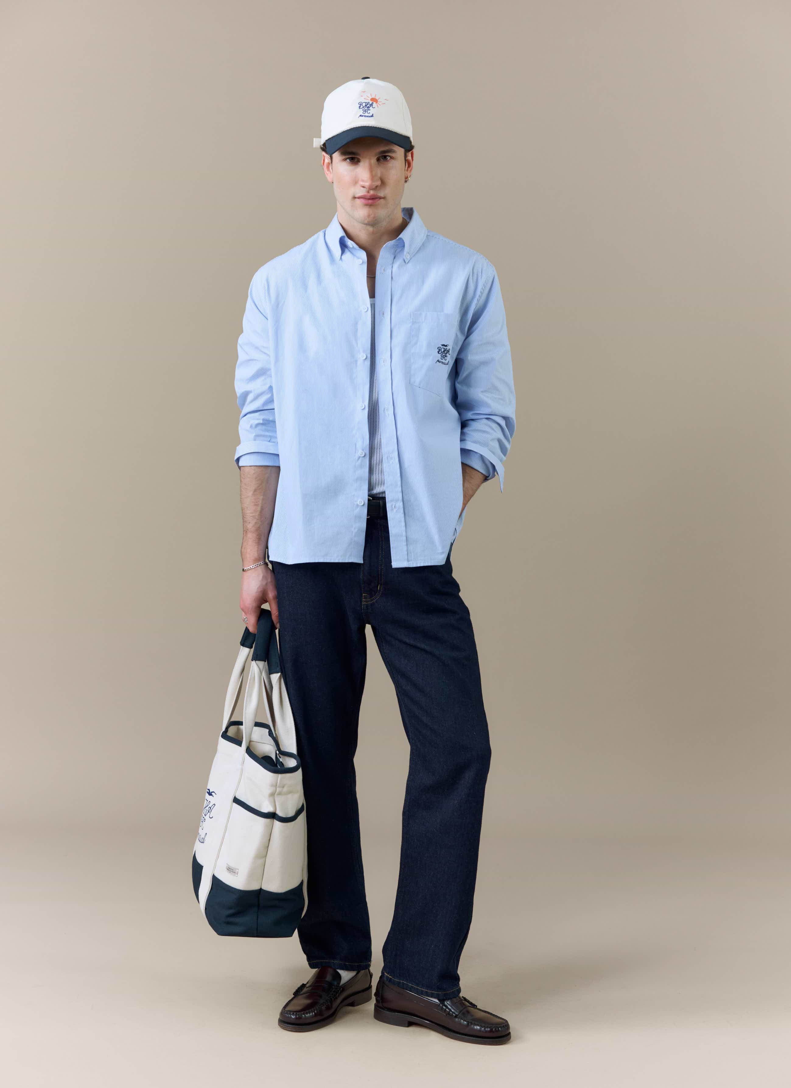 A model wears the full Percival x Brighton & Hove Albion F.C. look, including the Striped Pearce Shirt, cap and tote bag.