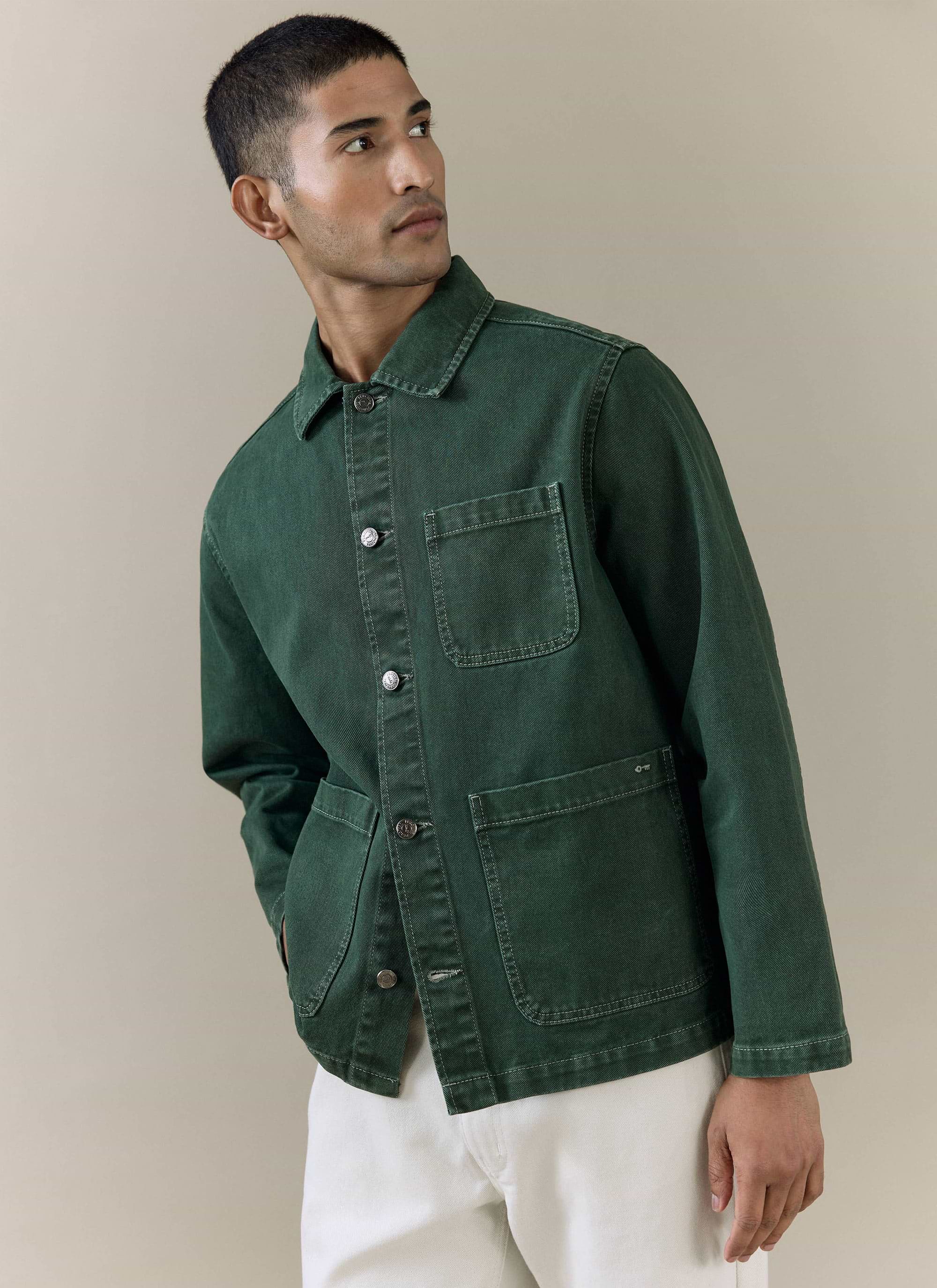 A model wears the forest green Percival Vintage Wash Oliver Chore Jacket in cotton canvas with white trousers.