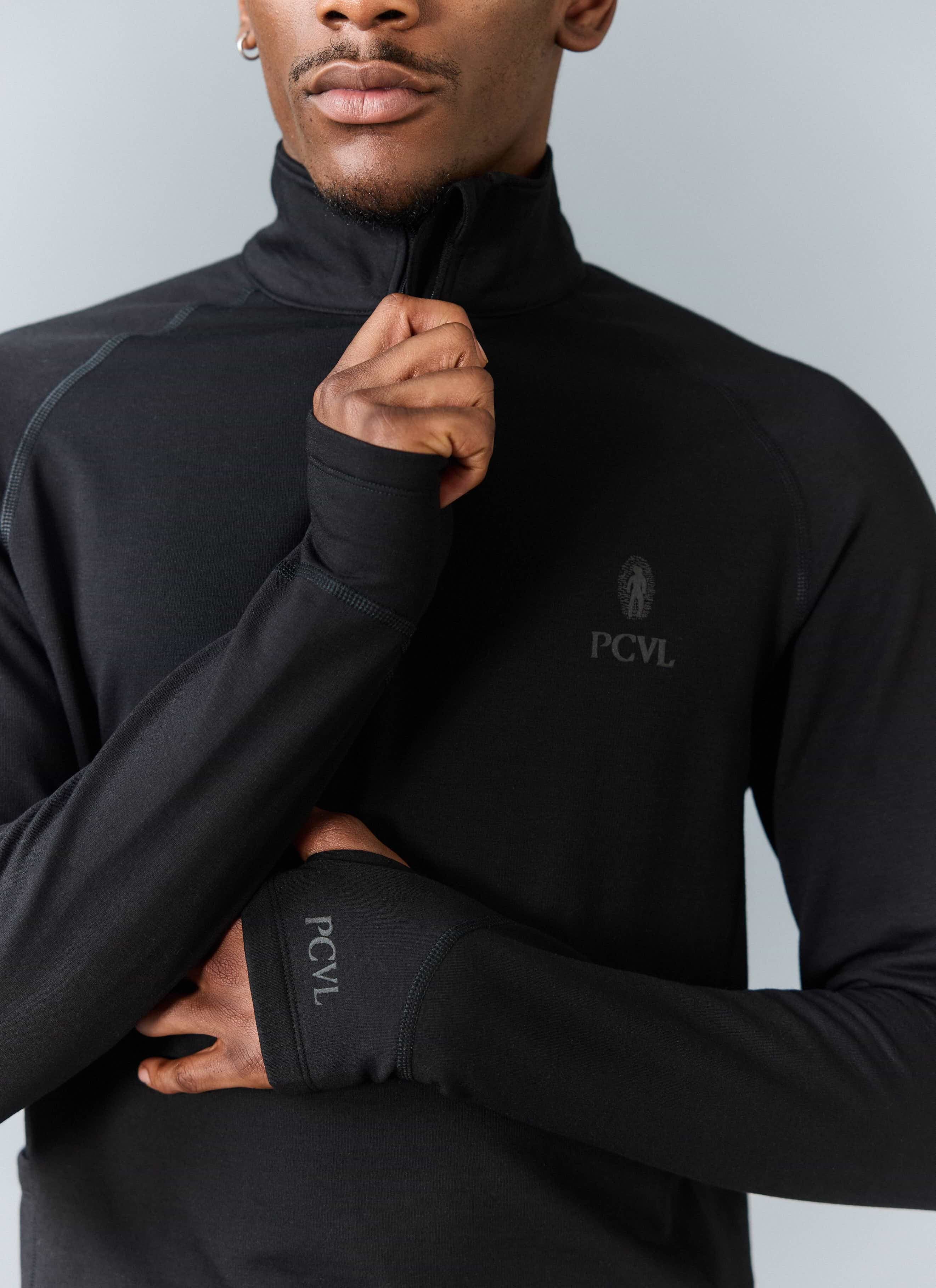 Close-up of a model wearing the black PCVL Base Layer Quarter Zip from Percival, showing the funnel neck and thumbhole cuff.