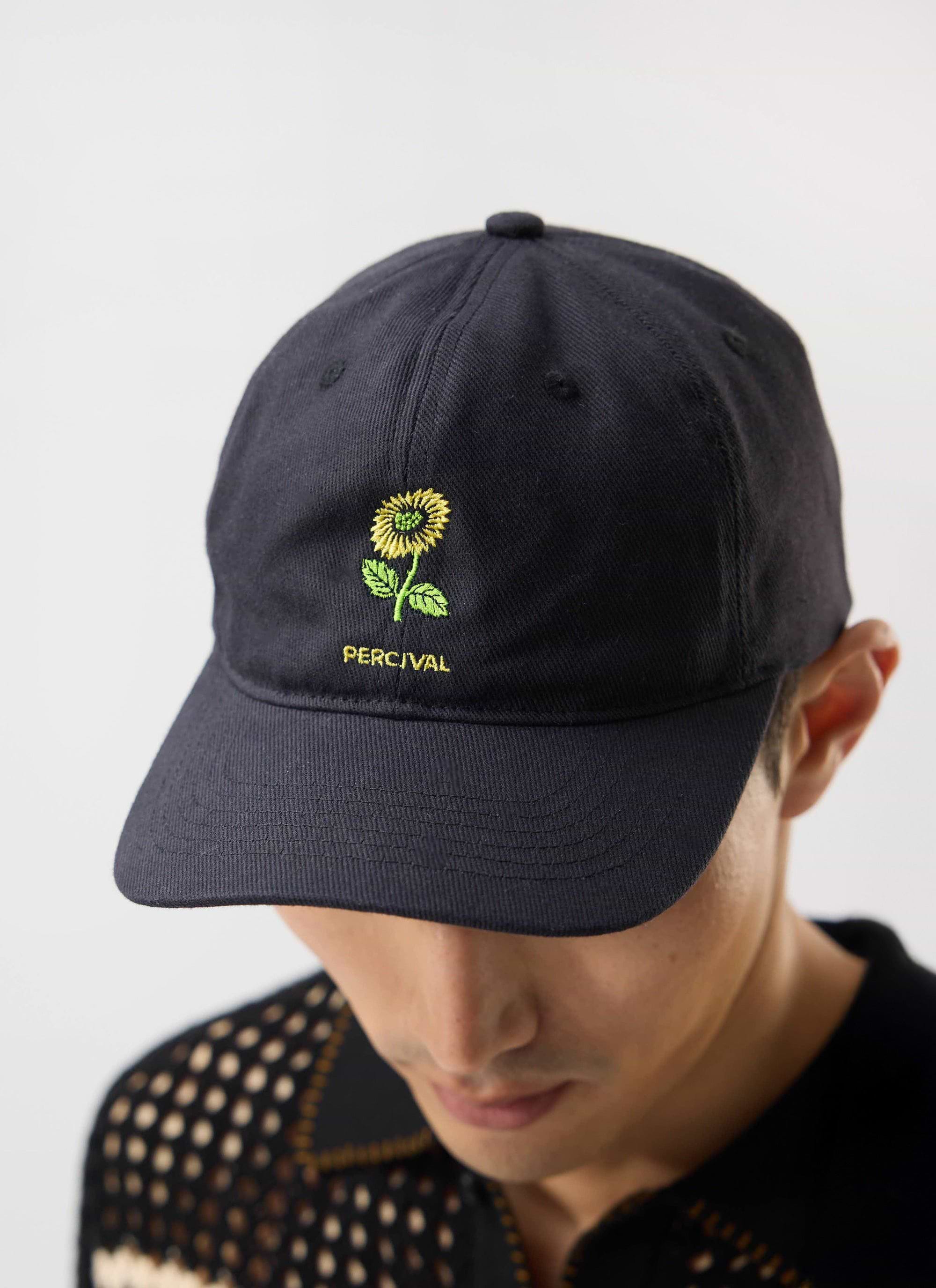 Close up of a model wearing the black Percival Nature Reserve cap, featuring a detailed yellow sunflower embroidery.
