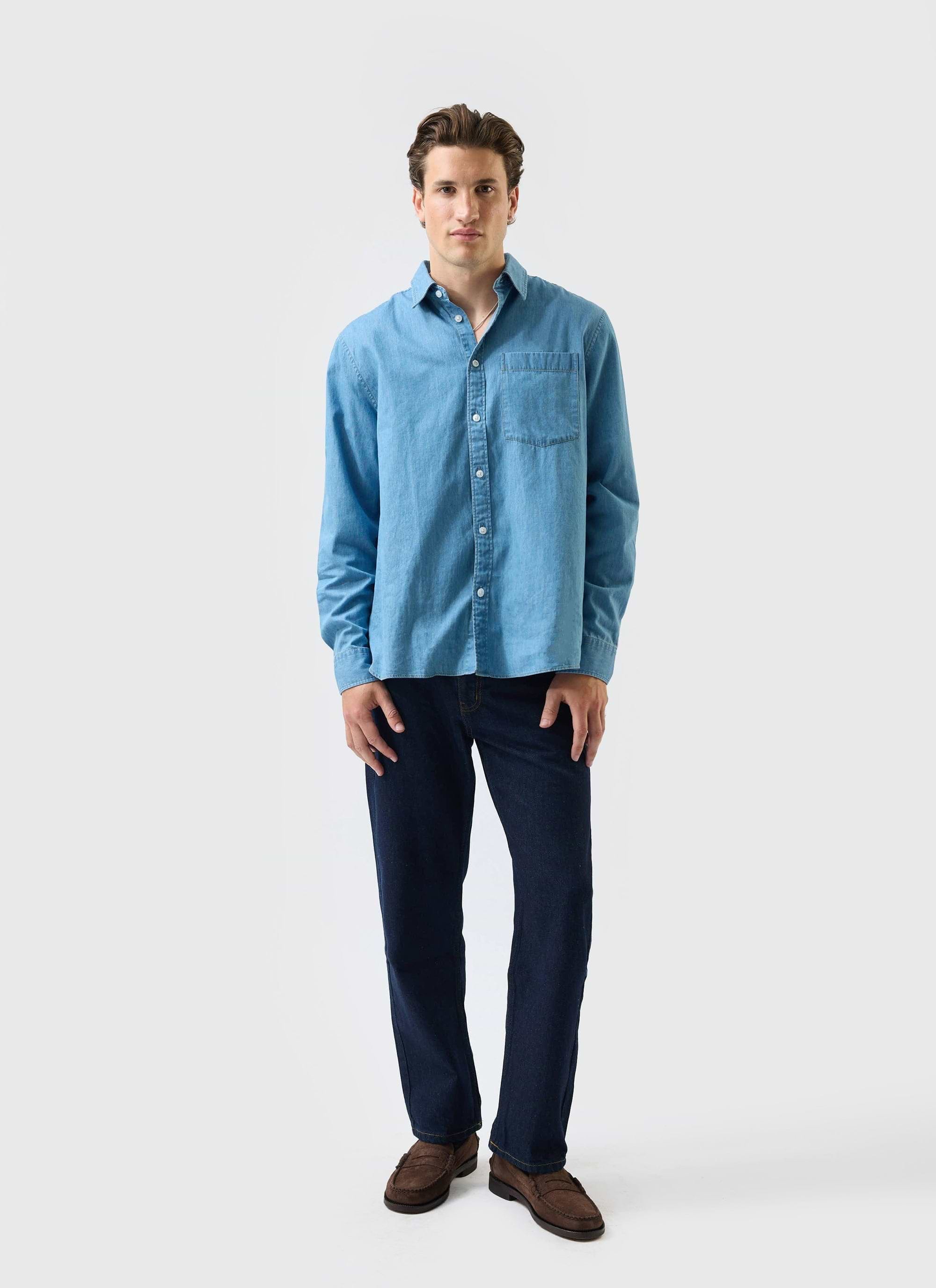 A man models the Percival Marco Pearce denim shirt in light wash blue, paired with dark jeans and brown loafers.
