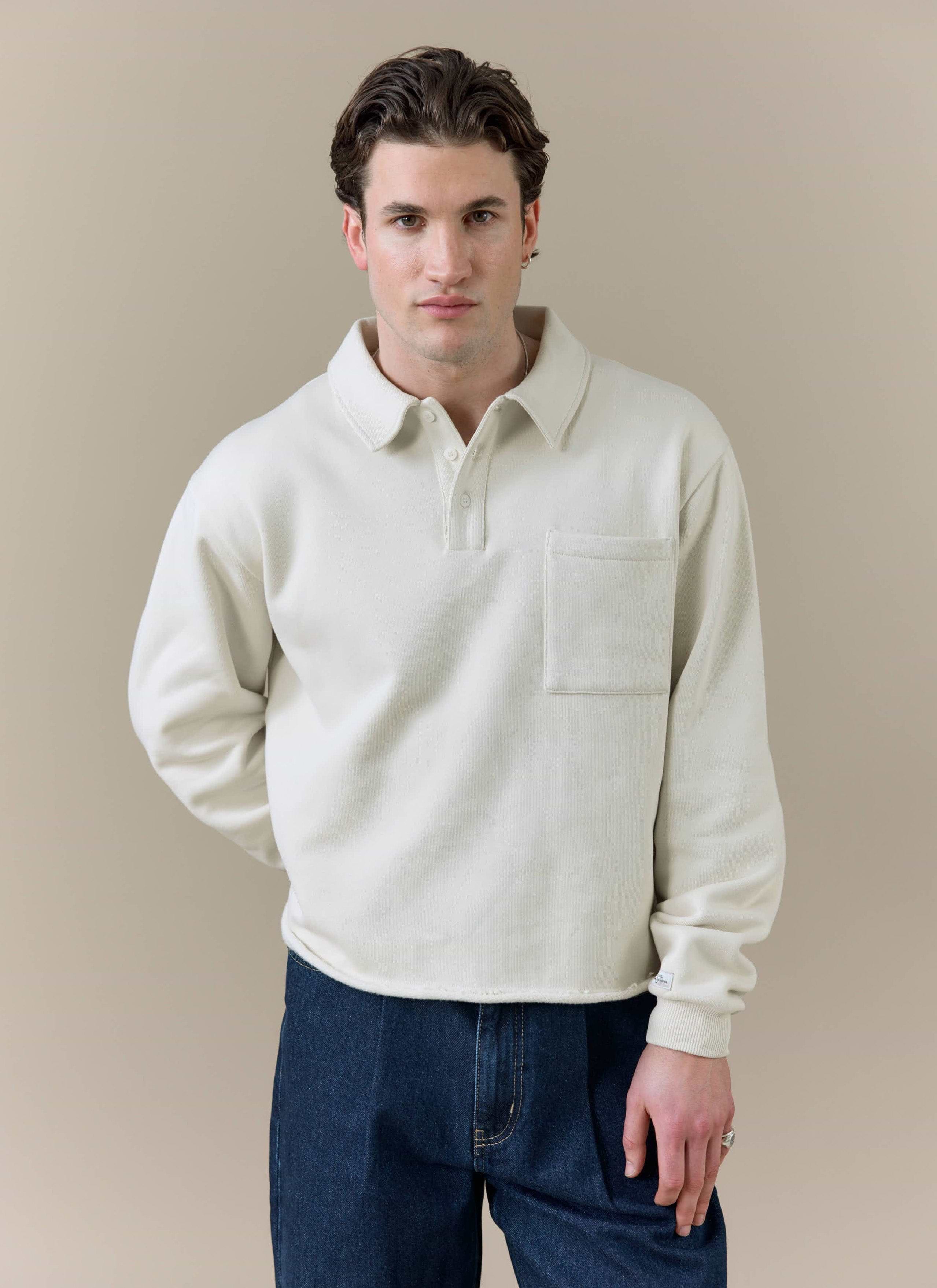A model wearing the cream Dudley Boxy Sweatshirt by Percival, featuring a polo collar and chest pocket.