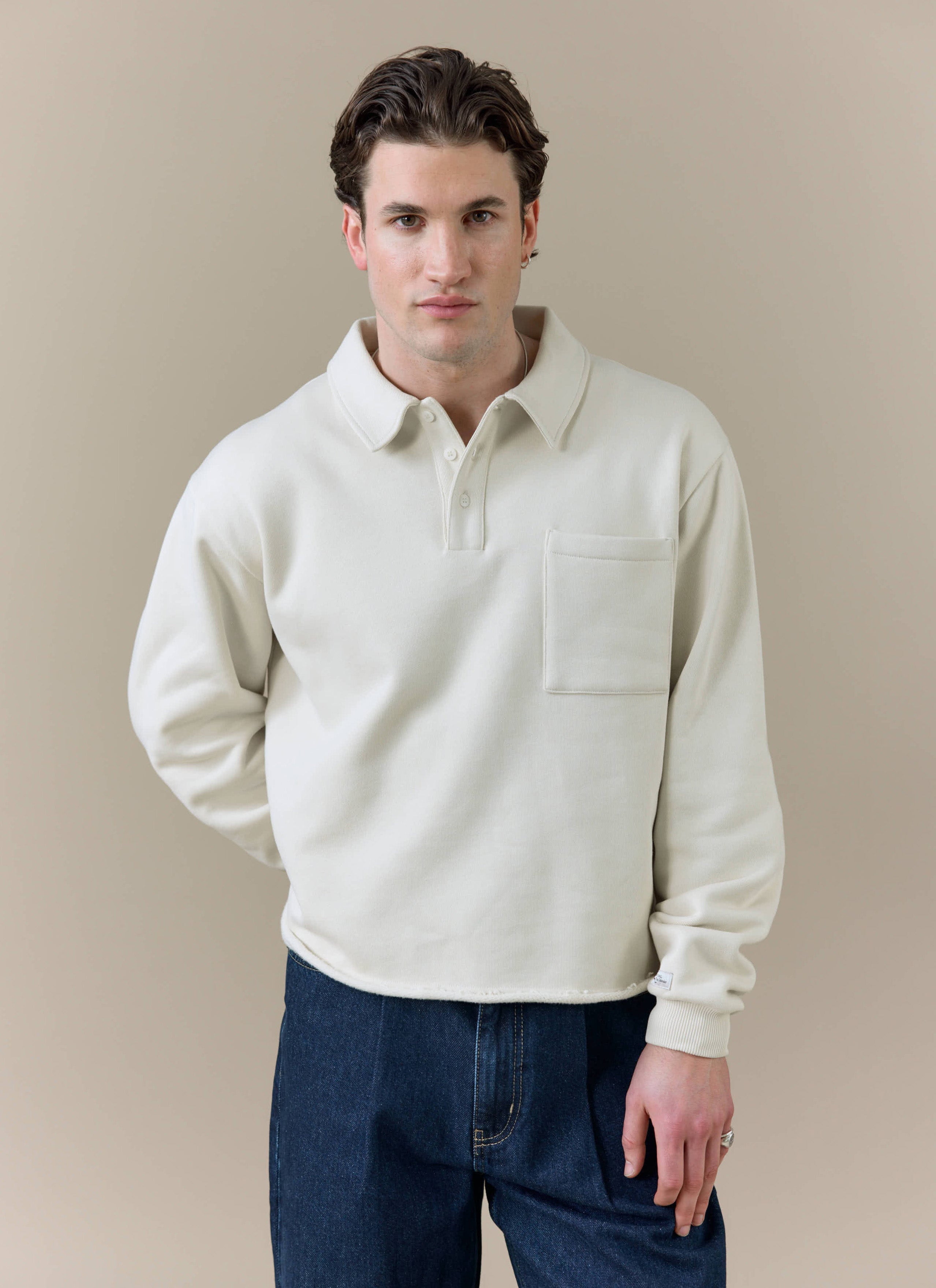 A model wearing the cream Dudley Boxy Sweatshirt by Percival, featuring a polo collar and chest pocket.
