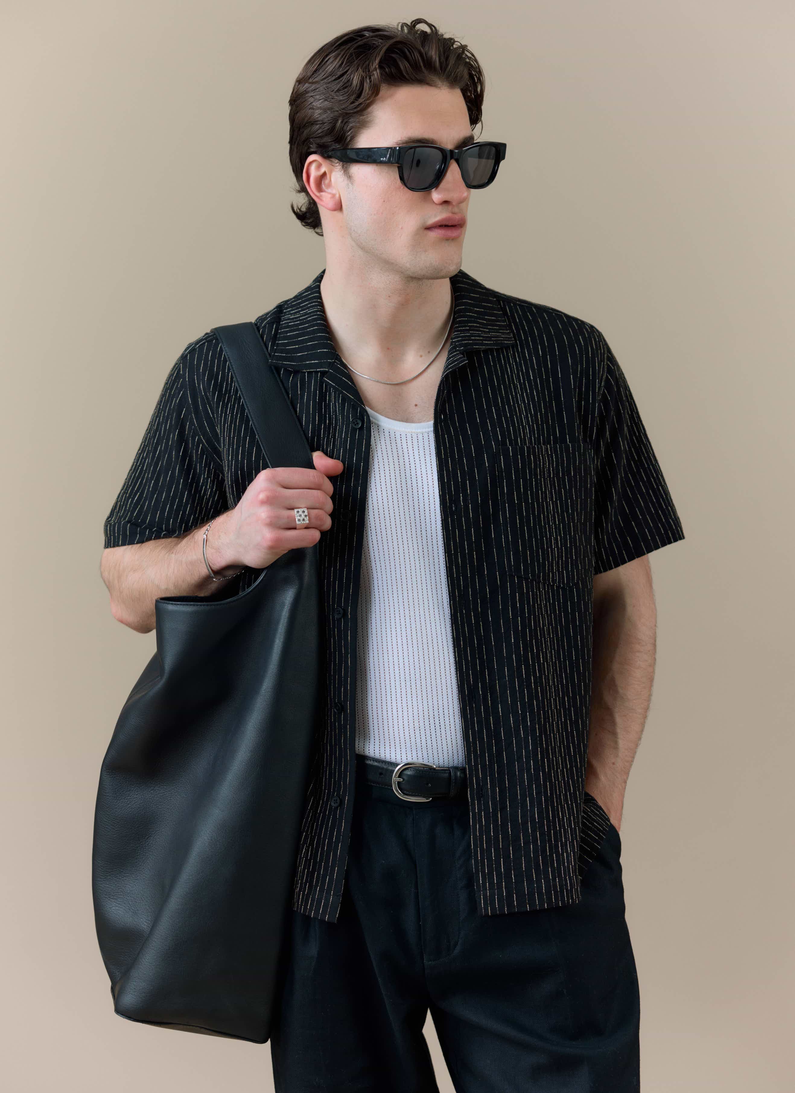 A model wearing the Percival Leland Cuban Shirt in black cotton with vertical stripes, styled open over a white vest.