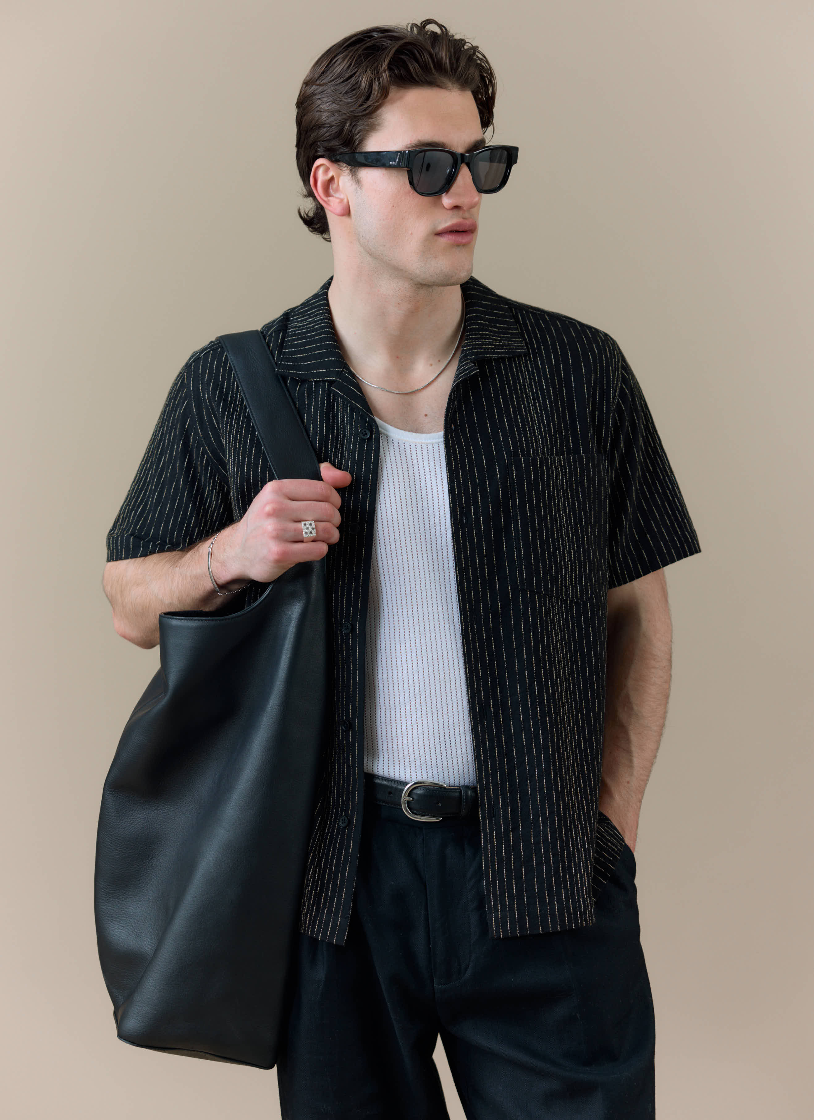 A model wearing the Percival Leland Cuban Shirt in black cotton with vertical stripes, styled open over a white vest.