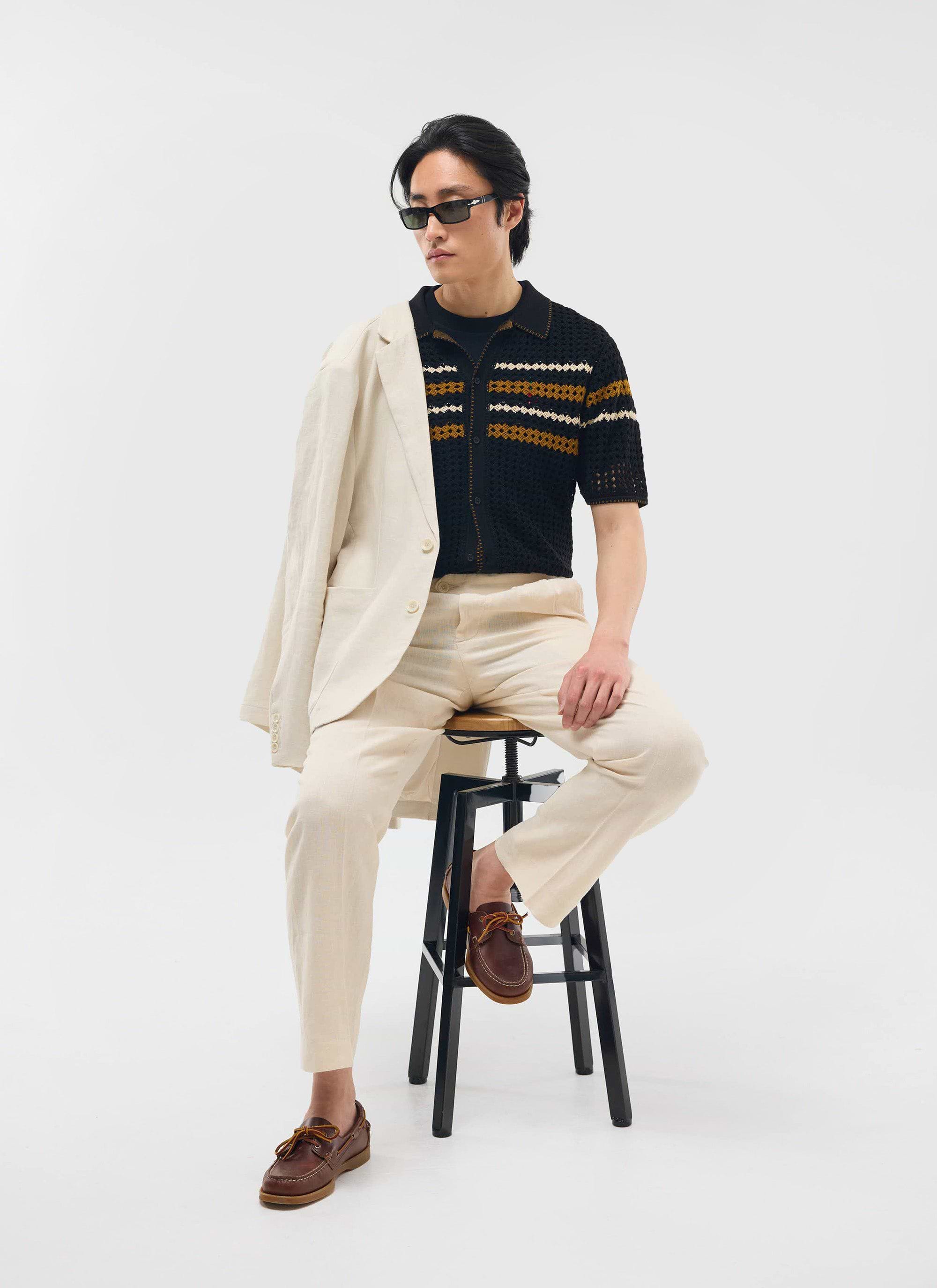 A model wears the black Percival Pesaro Knitted Shirt, styled with cream trousers and a blazer draped over his shoulder.
