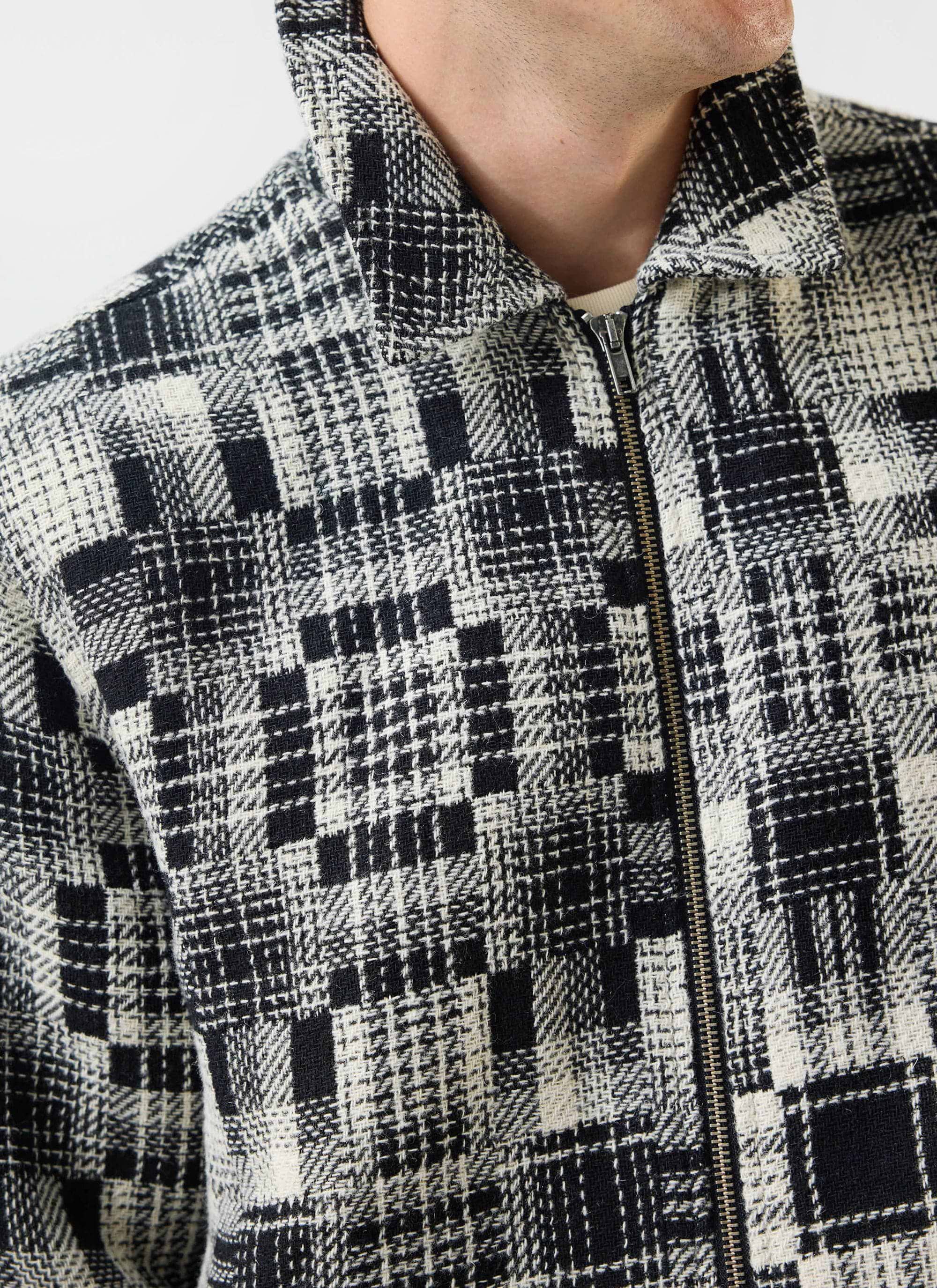 Close up of a model wearing the Percival Glossary Patchwork Jacket in grey, showing the woven twill texture and zip detail.