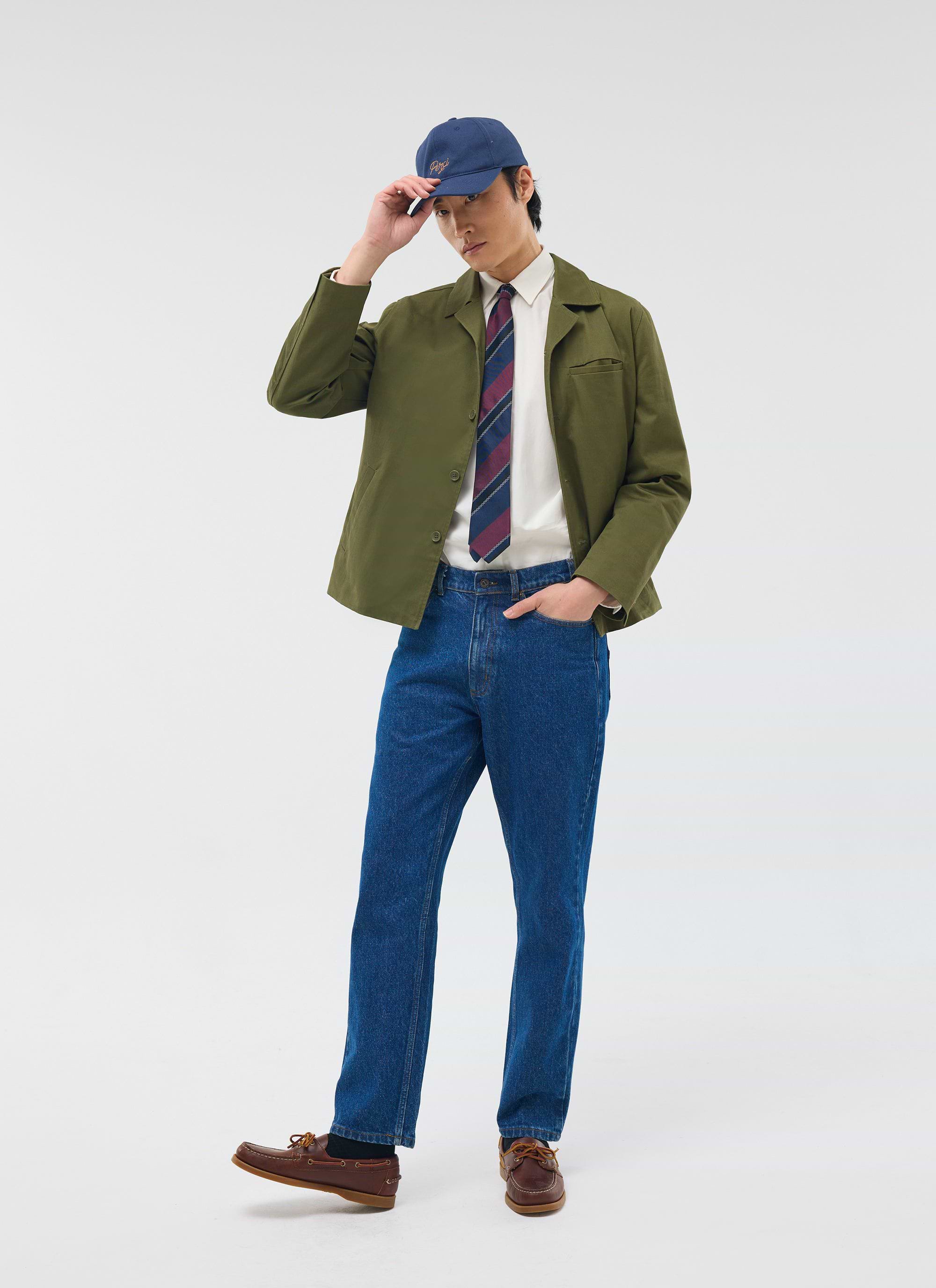 The Percival Casual Workwear Jacket in khaki, styled on a model with a shirt, tie, blue jeans and a baseball cap.