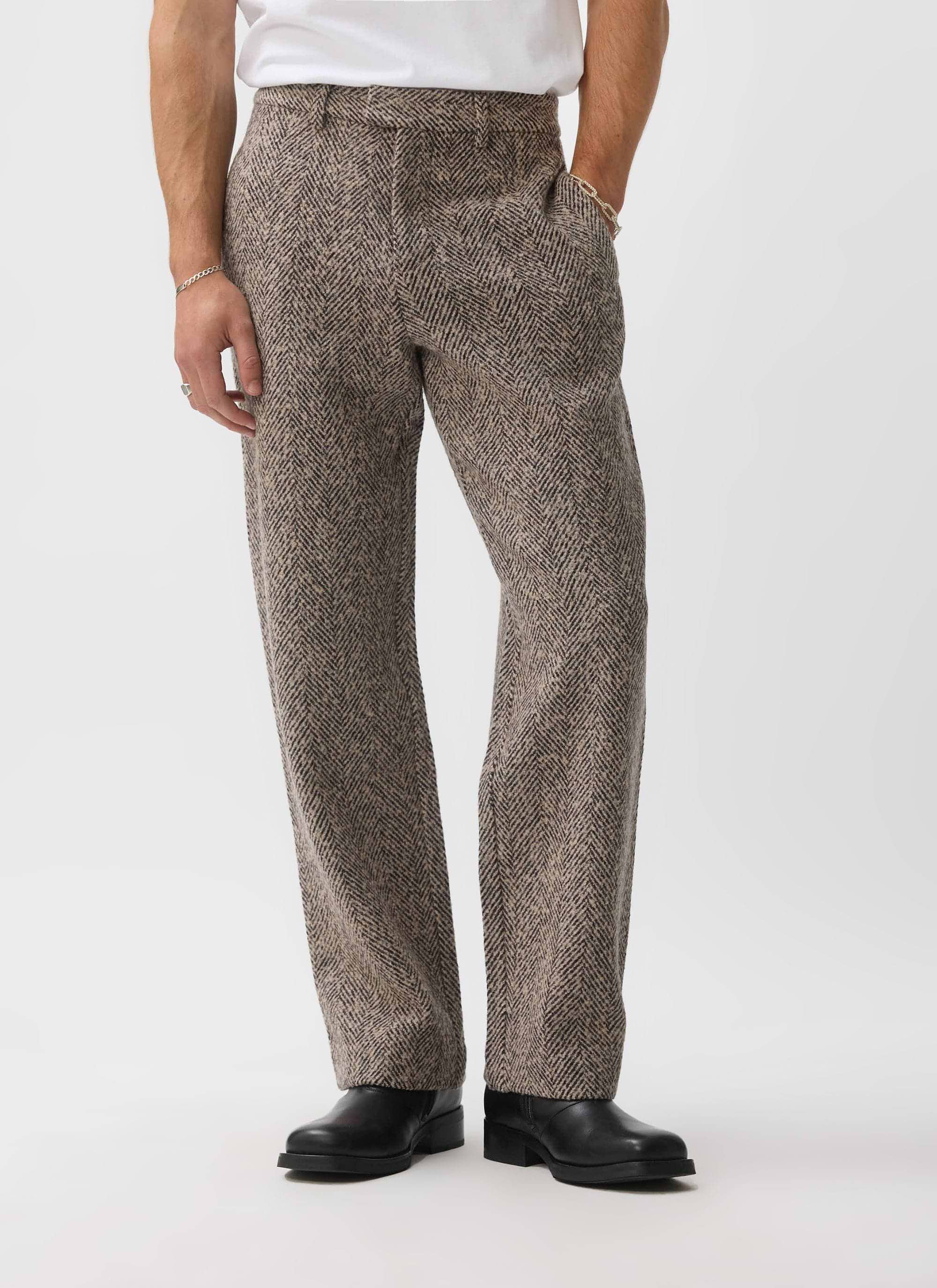 A man models the ecru wool Herringbone Trousers from Percival, paired with a white t-shirt and black boots.