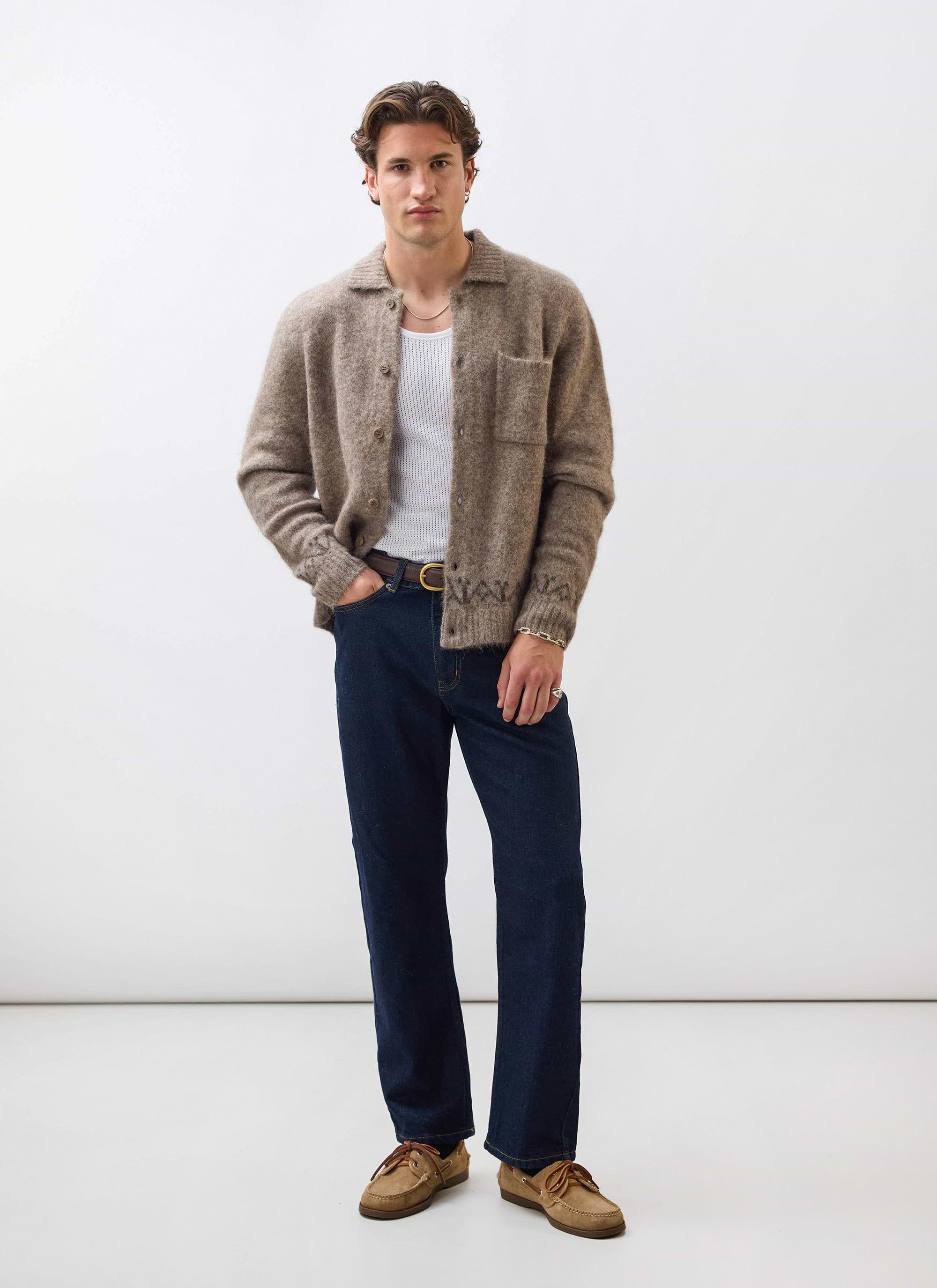 A model wears the Percival Novel Collared Cardigan in oak, styled over a white vest with dark jeans and loafers.