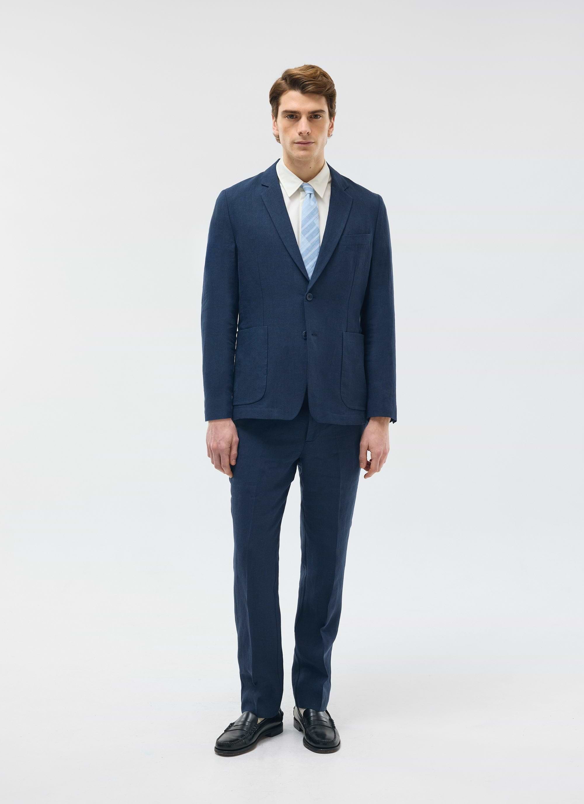 A model wears the Percival navy tailored linen trousers and matching blazer with a white shirt and light blue tie.
