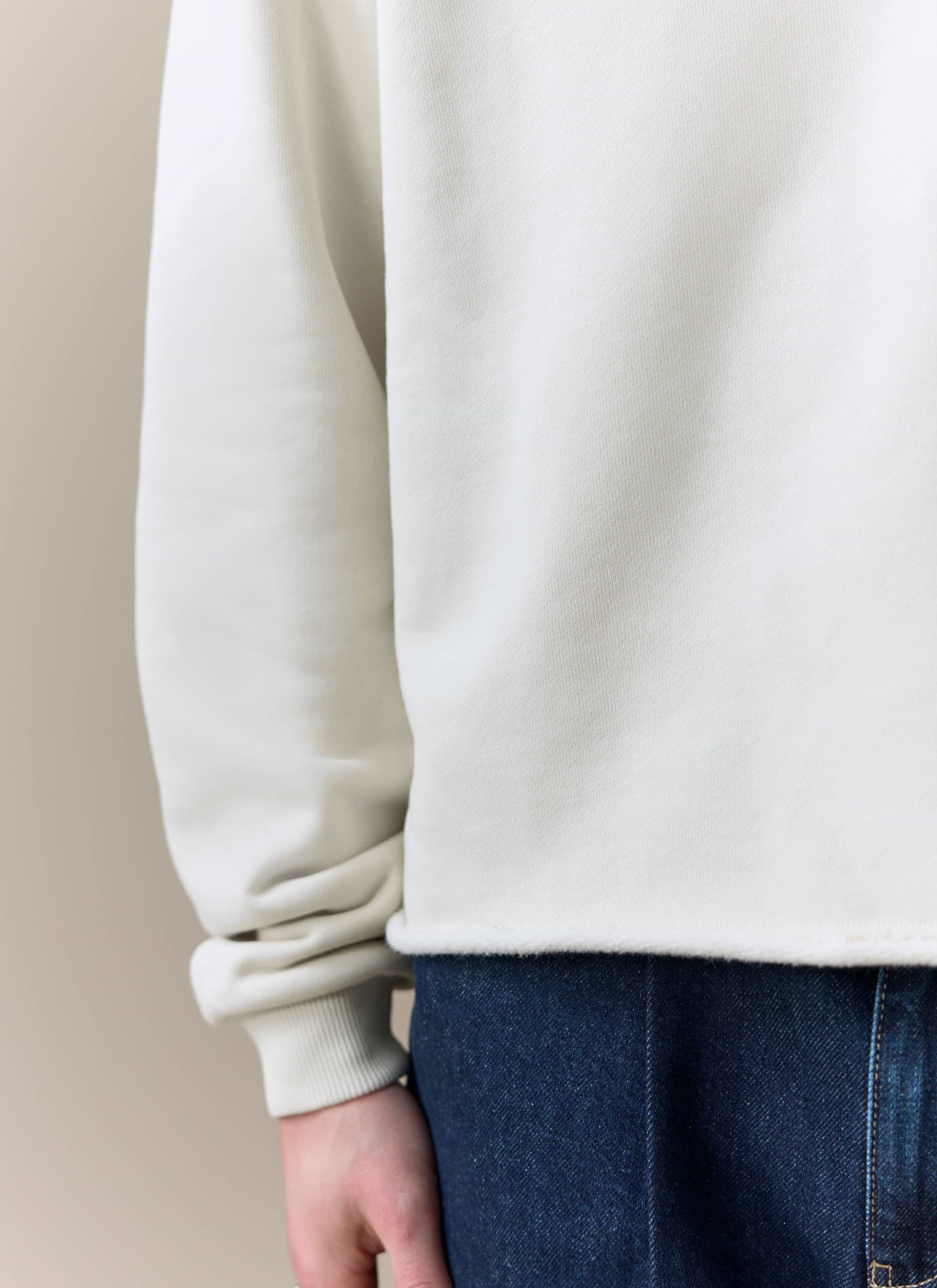 A close-up shot of the cream organic cotton fabric and raw hem of the Dudley Boxy Sweatshirt by Percival.