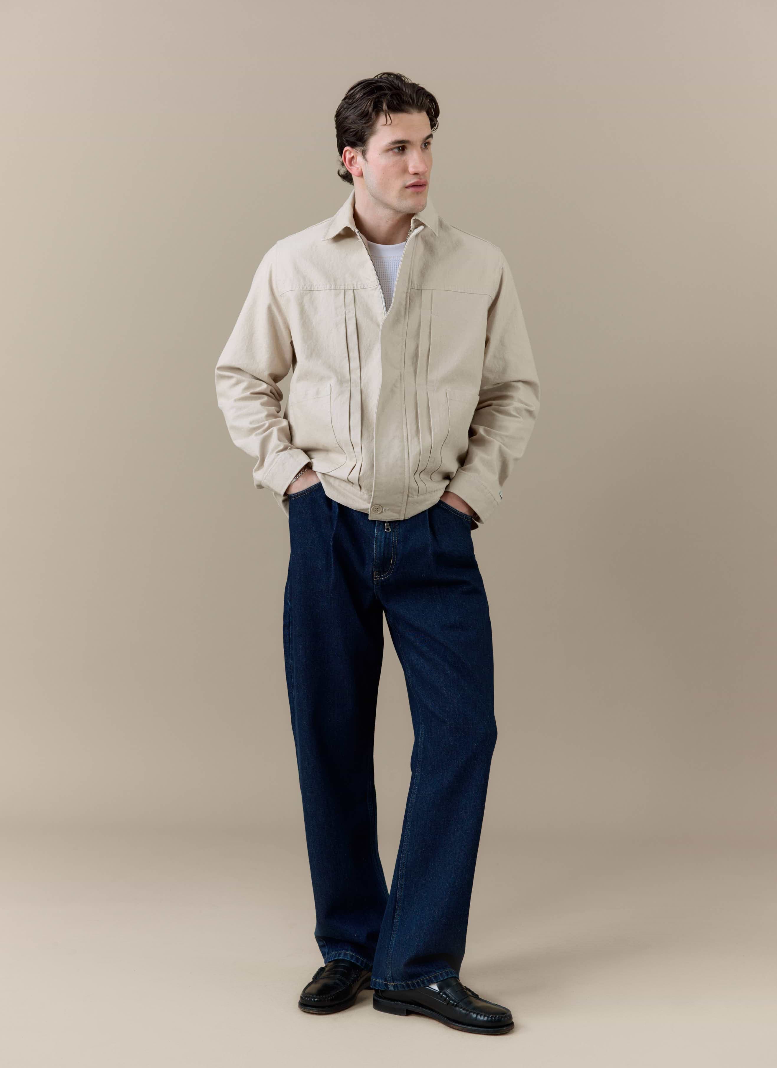 A model wearing the cream cotton Ernst Jacket by Percival, styled with dark blue denim trousers and black loafers.