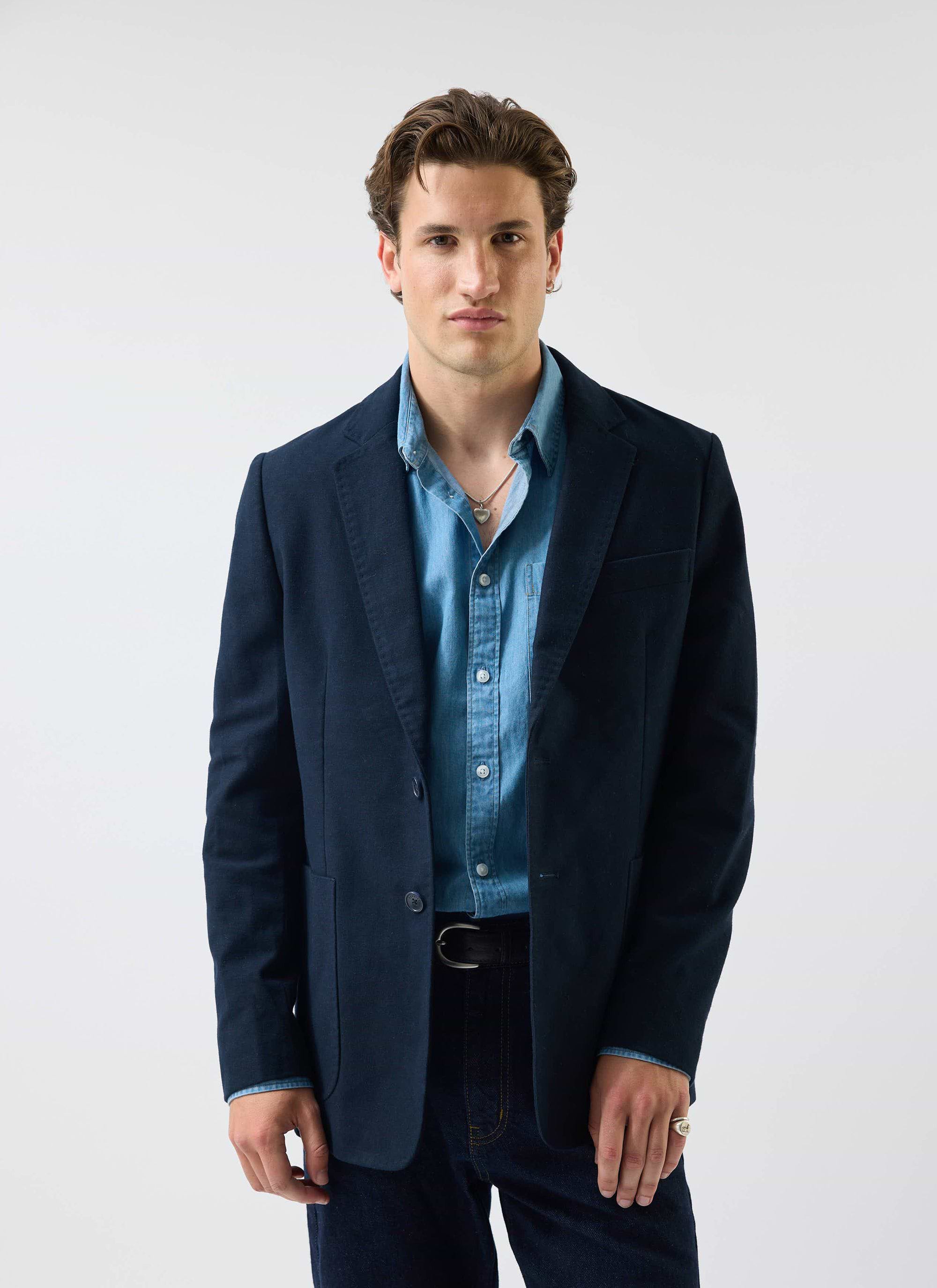 A model wears the Percival Marco Pearce light wash denim shirt, layered under a dark navy blazer for a smart-casual look.