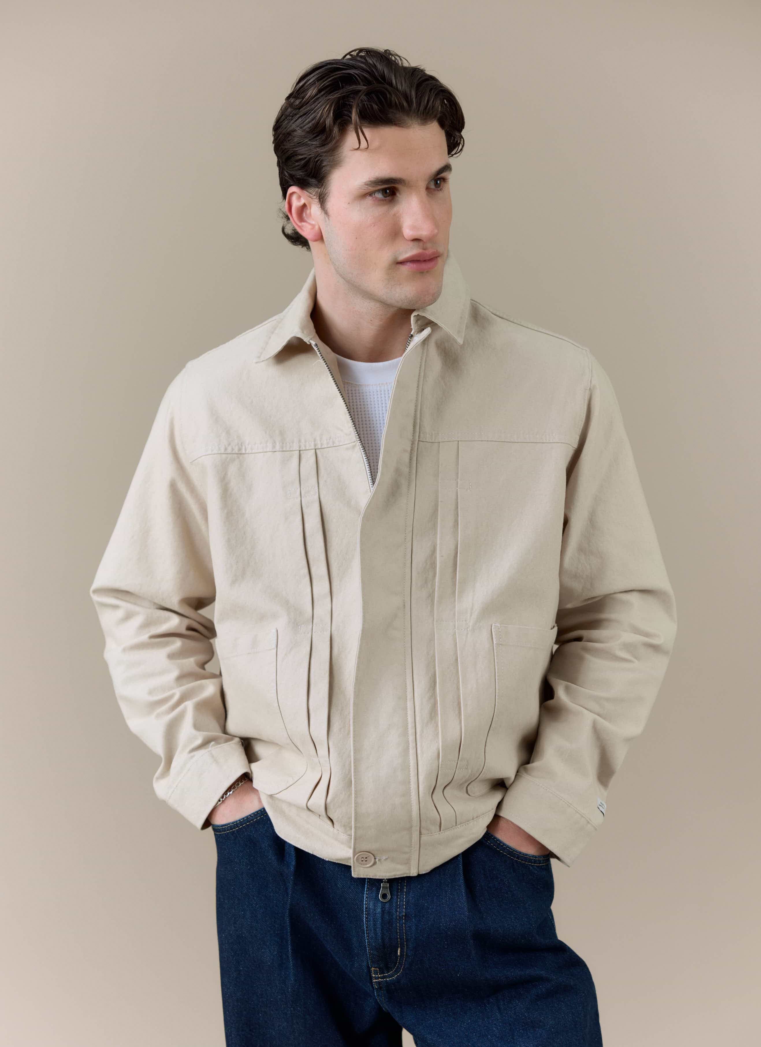 Model wearing the cream Ernst Jacket by Percival, featuring double pleated front detailing and zip fastening.