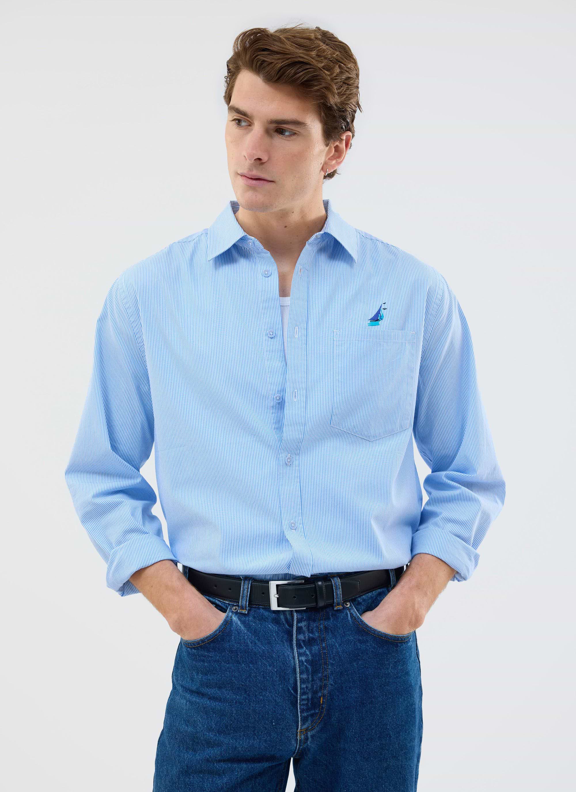 A model wears the Percival Yacht Stripe Oversized Shirt in blue, styled with dark denim jeans against a plain background.