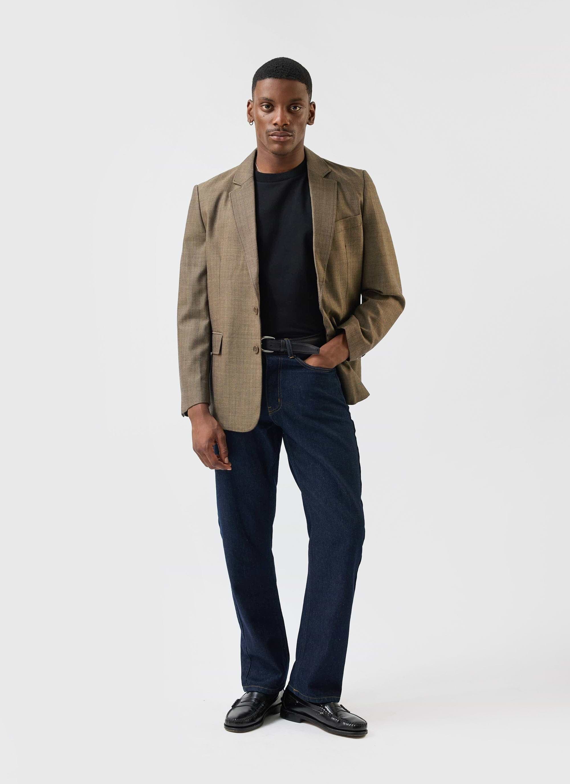 A model wears the Percival Grounds Tailored Blazer in oak herringbone, styled casually with dark denim and a black t-shirt.