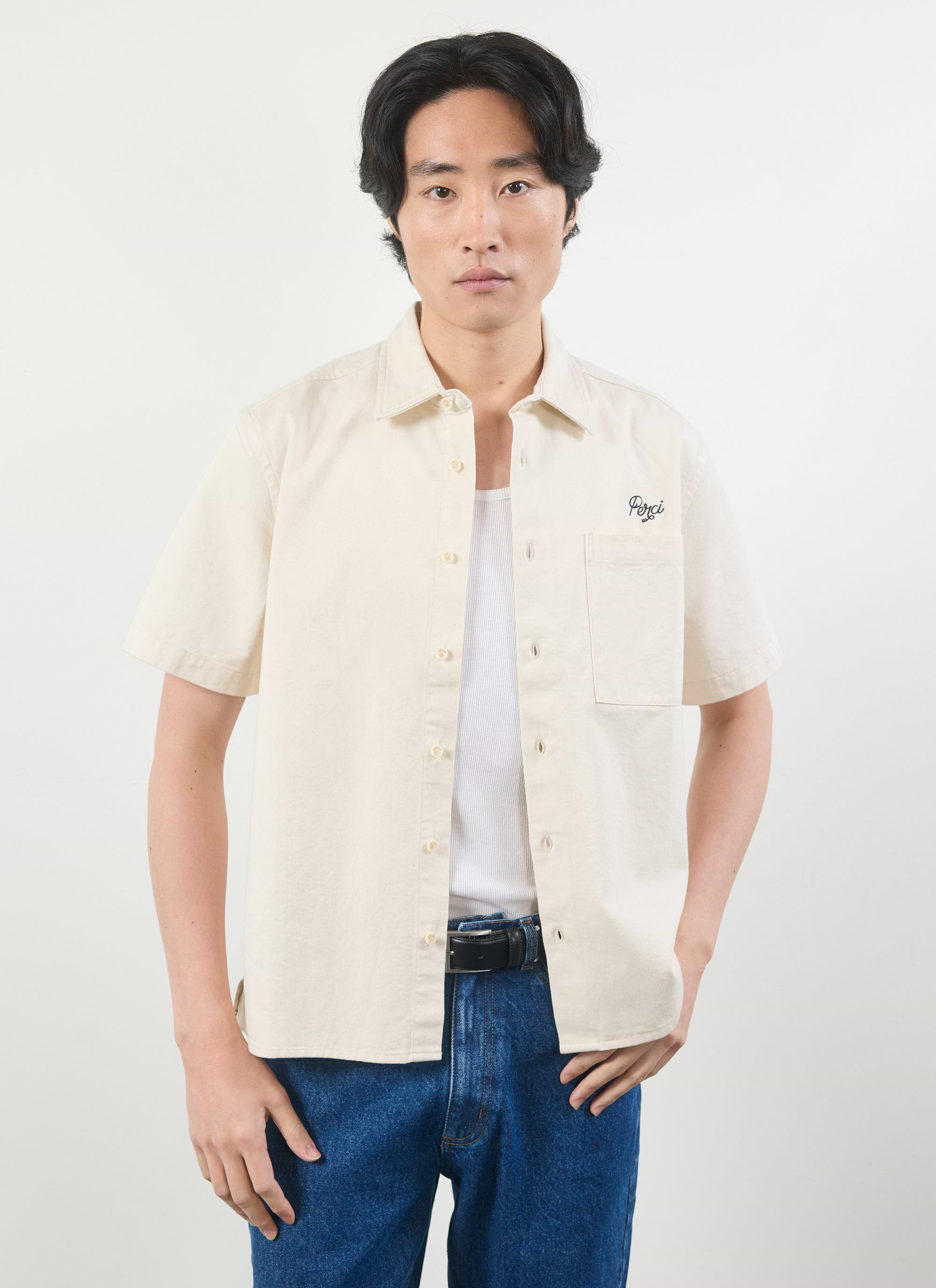 A model wears the Percival Olive Embroidered Cropped Shirt in off-white, styled open over a vest and blue jeans.