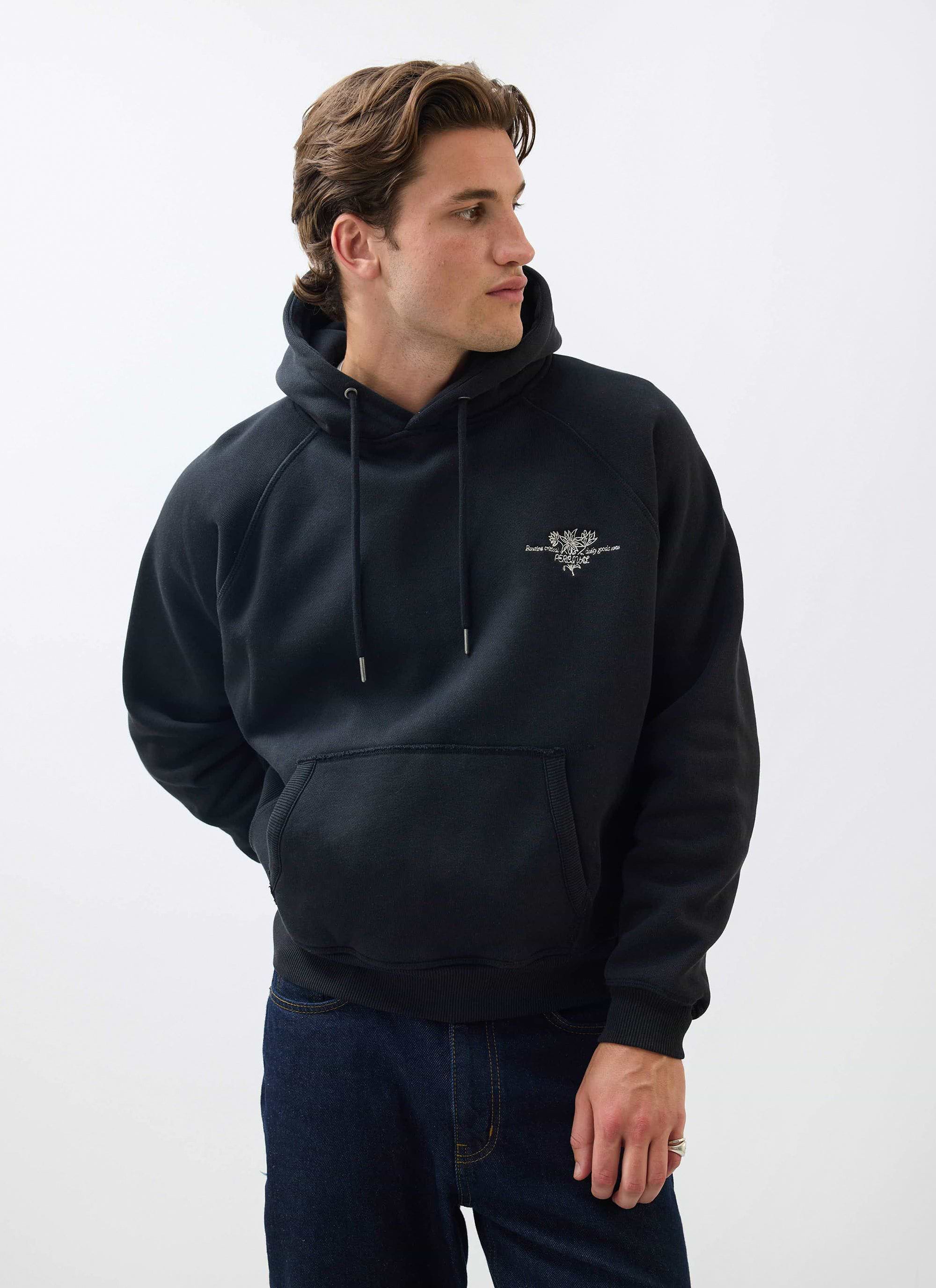 A model wears the black cotton Heritage 90's Raglan Hoodie from Percival against a white studio background.