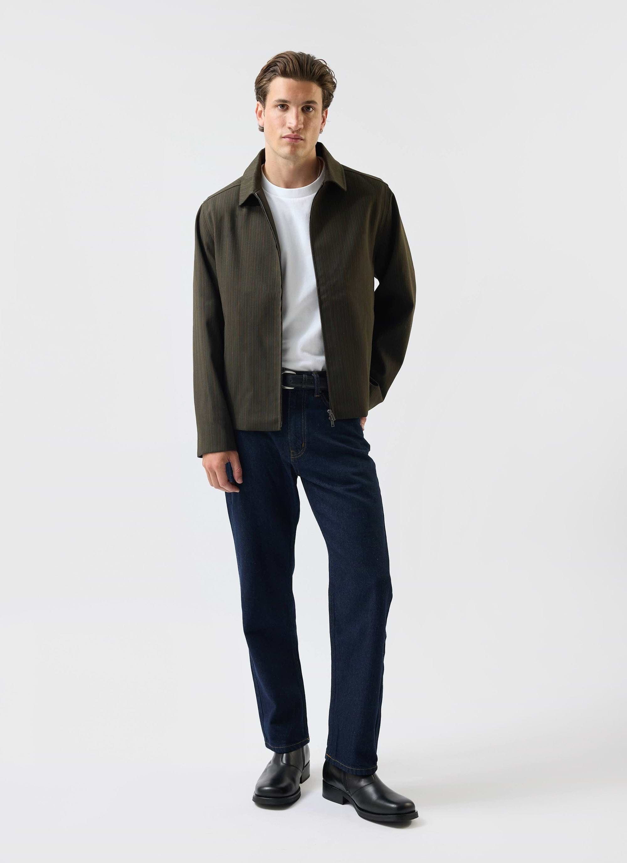 A man models the Percival Chapter Zip Up Jacket in forest green, styled with a white t-shirt and dark denim jeans.