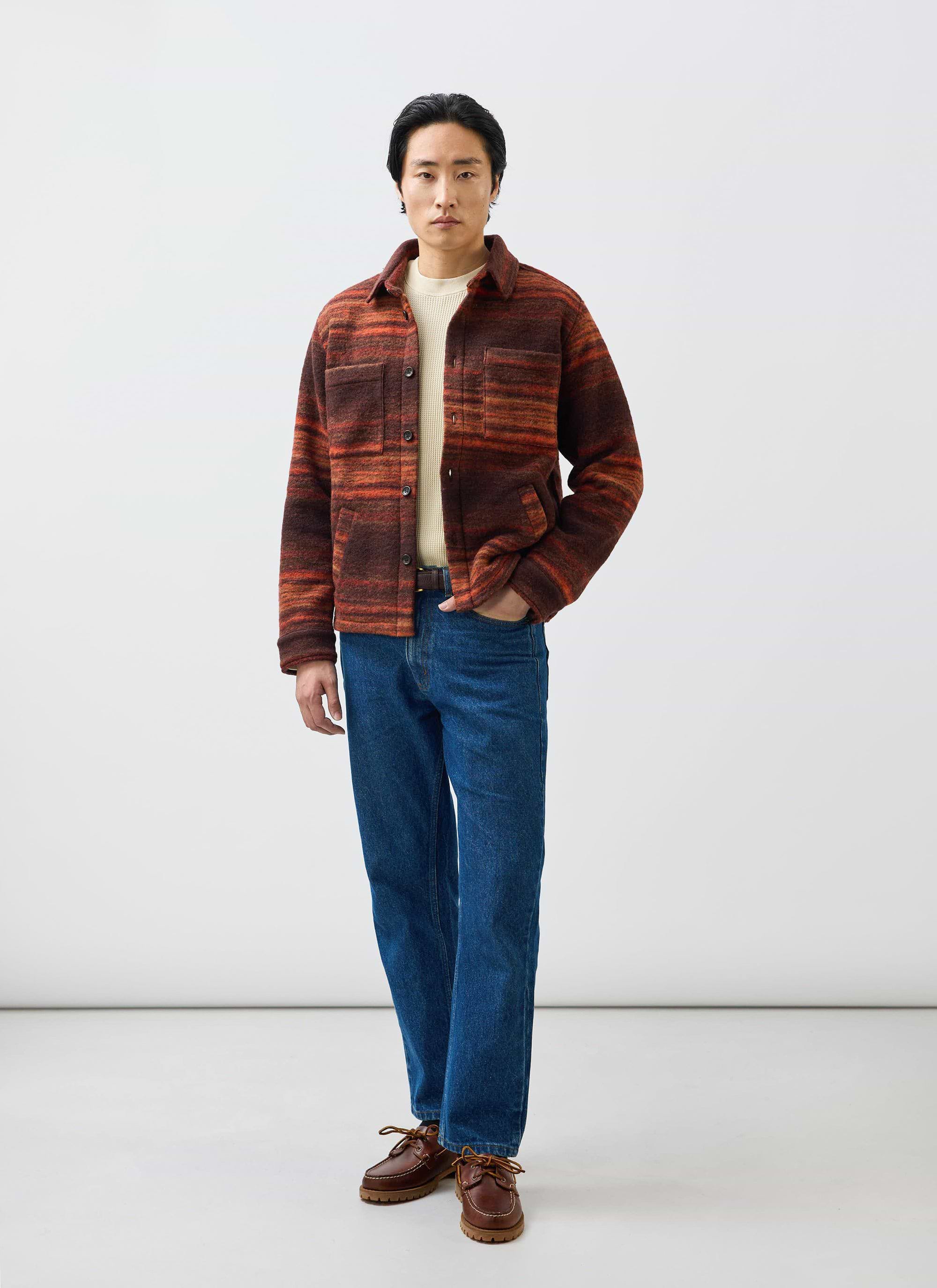 A model wears the Percival Mississippi Jacquard Overshirt in burnt orange and brown, styled with blue jeans and a cream knit.