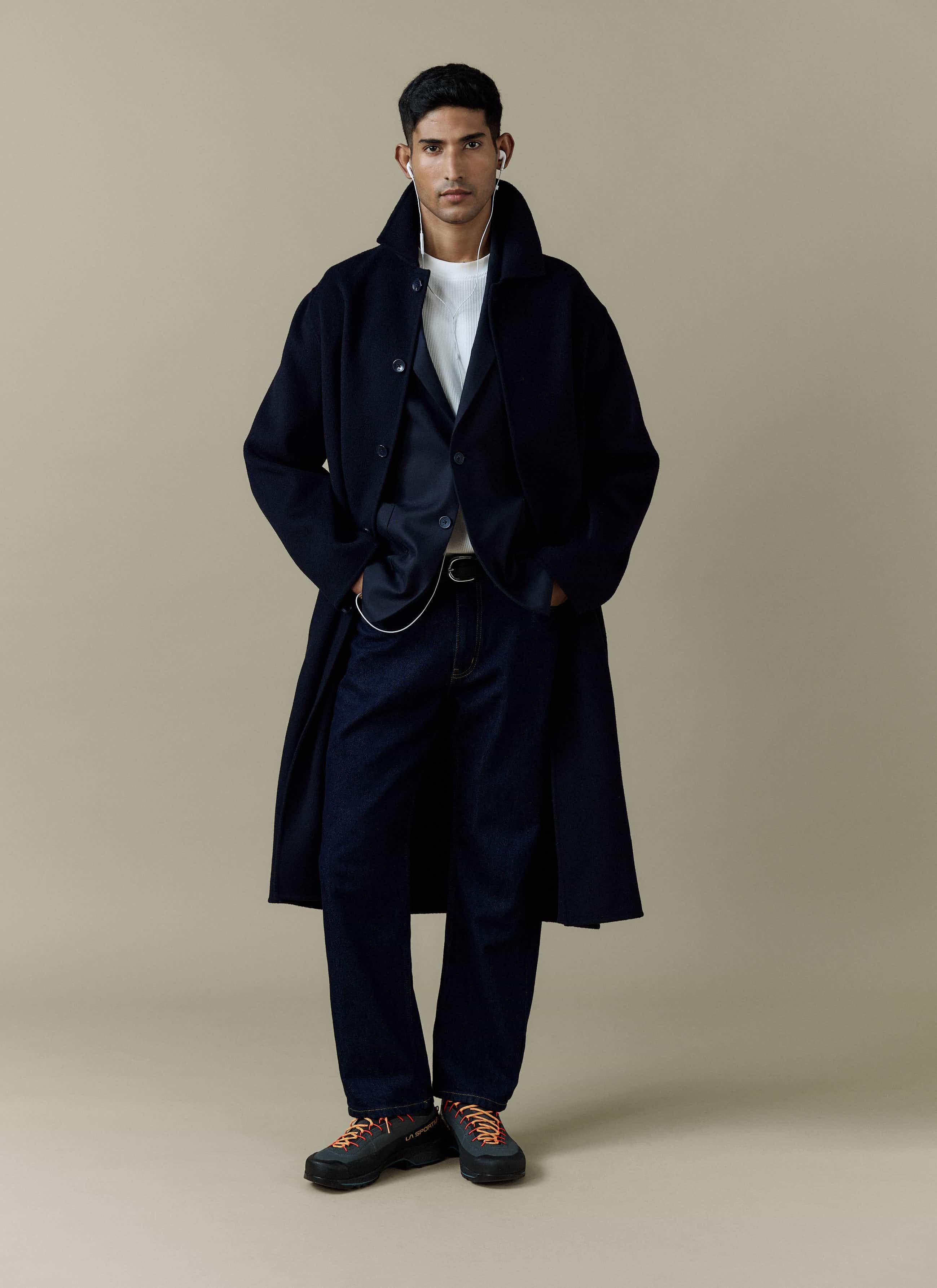 A model layers the navy Lyocell Blazer and waistcoat from Percival under a long coat, styled with dark jeans and trainers.