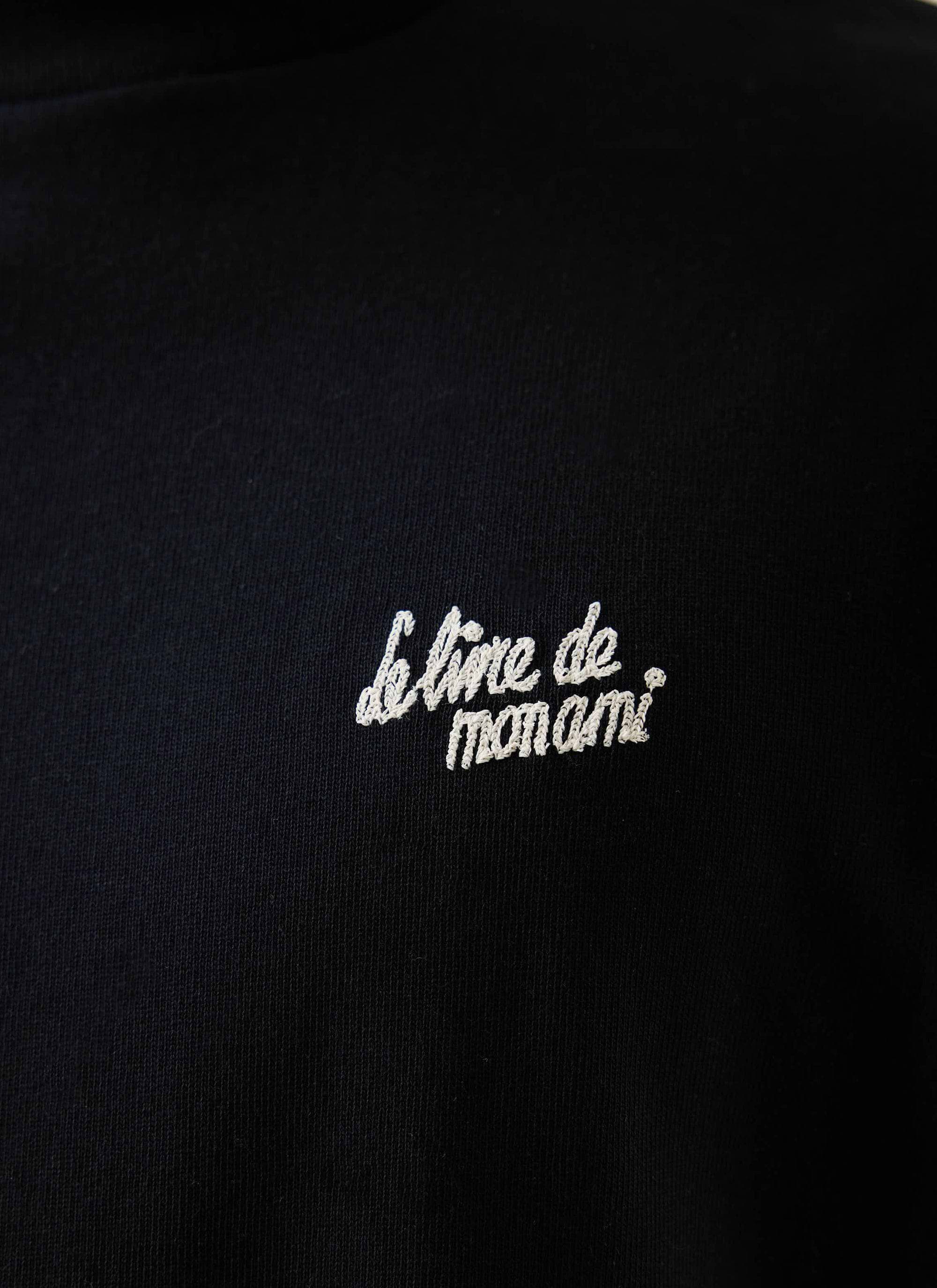 Close-up of the 'Le Livre de mon ami' embroidery on the chest of the black cotton t-shirt from Percival.