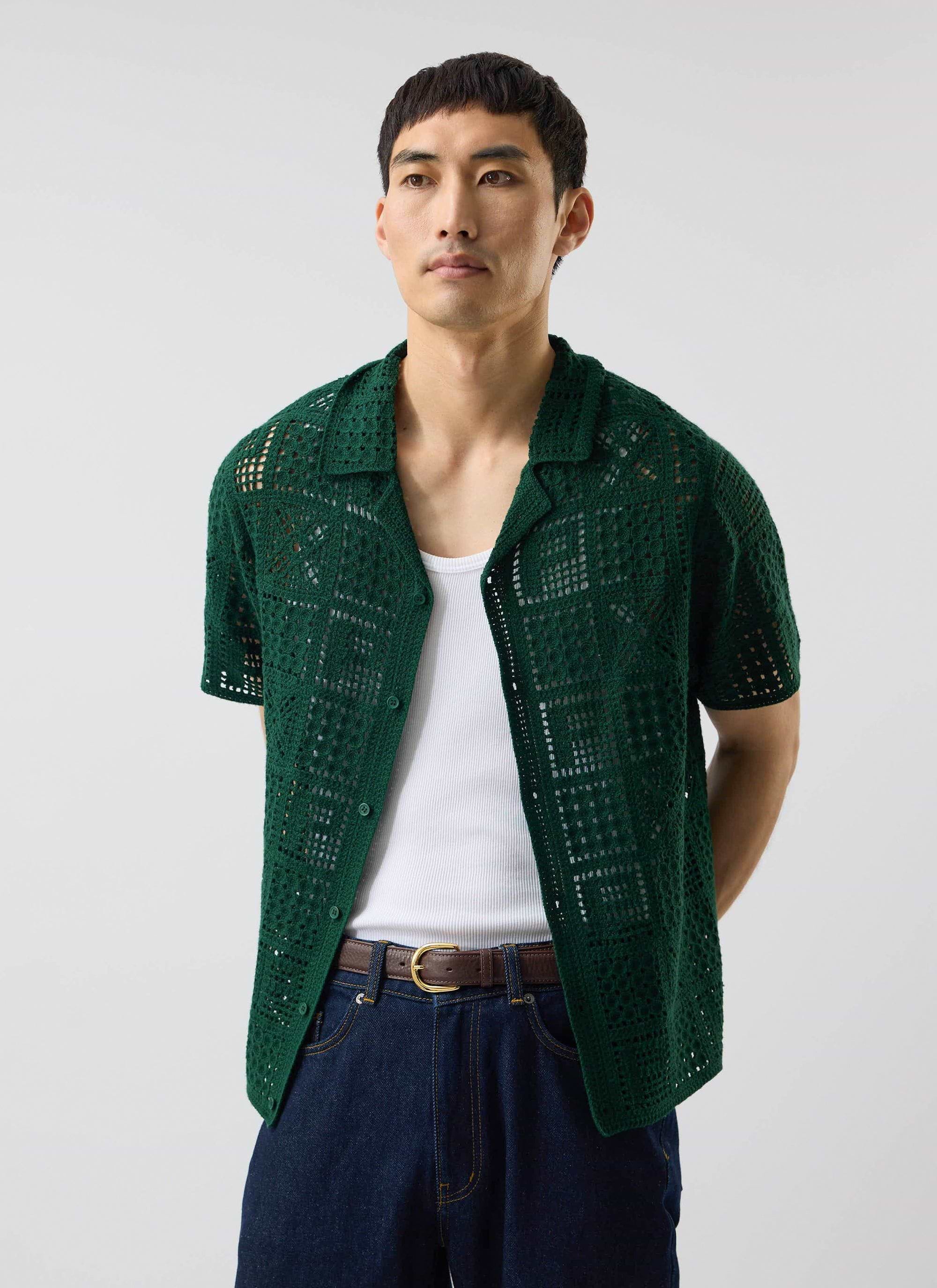 A model wears the Percival Crochet Groundsman Shirt in forest green, layered over a white vest and styled with dark jeans.