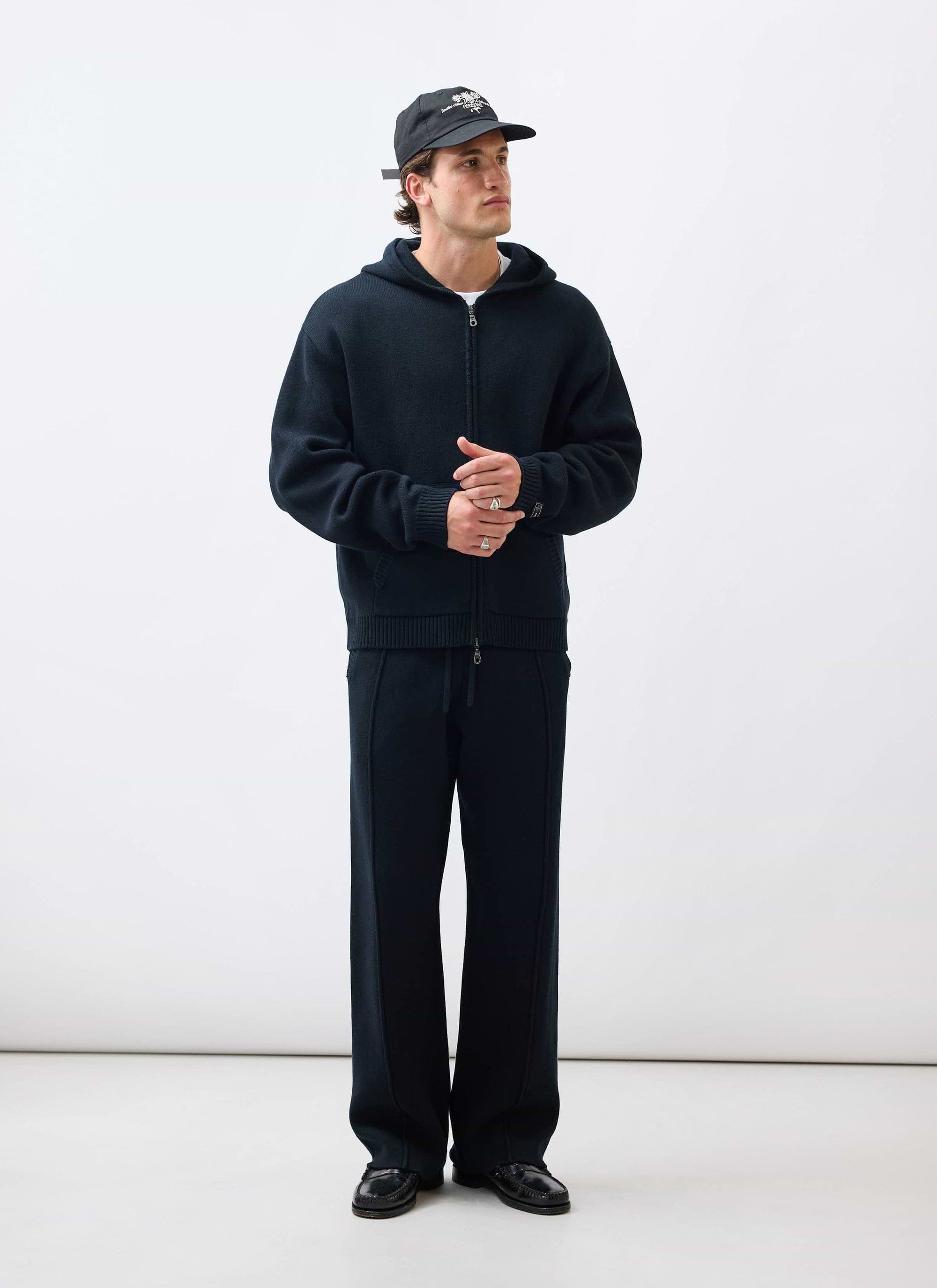 A model wears the black Chronicle Knitted Hoodie with matching trousers from Percival against a white background.