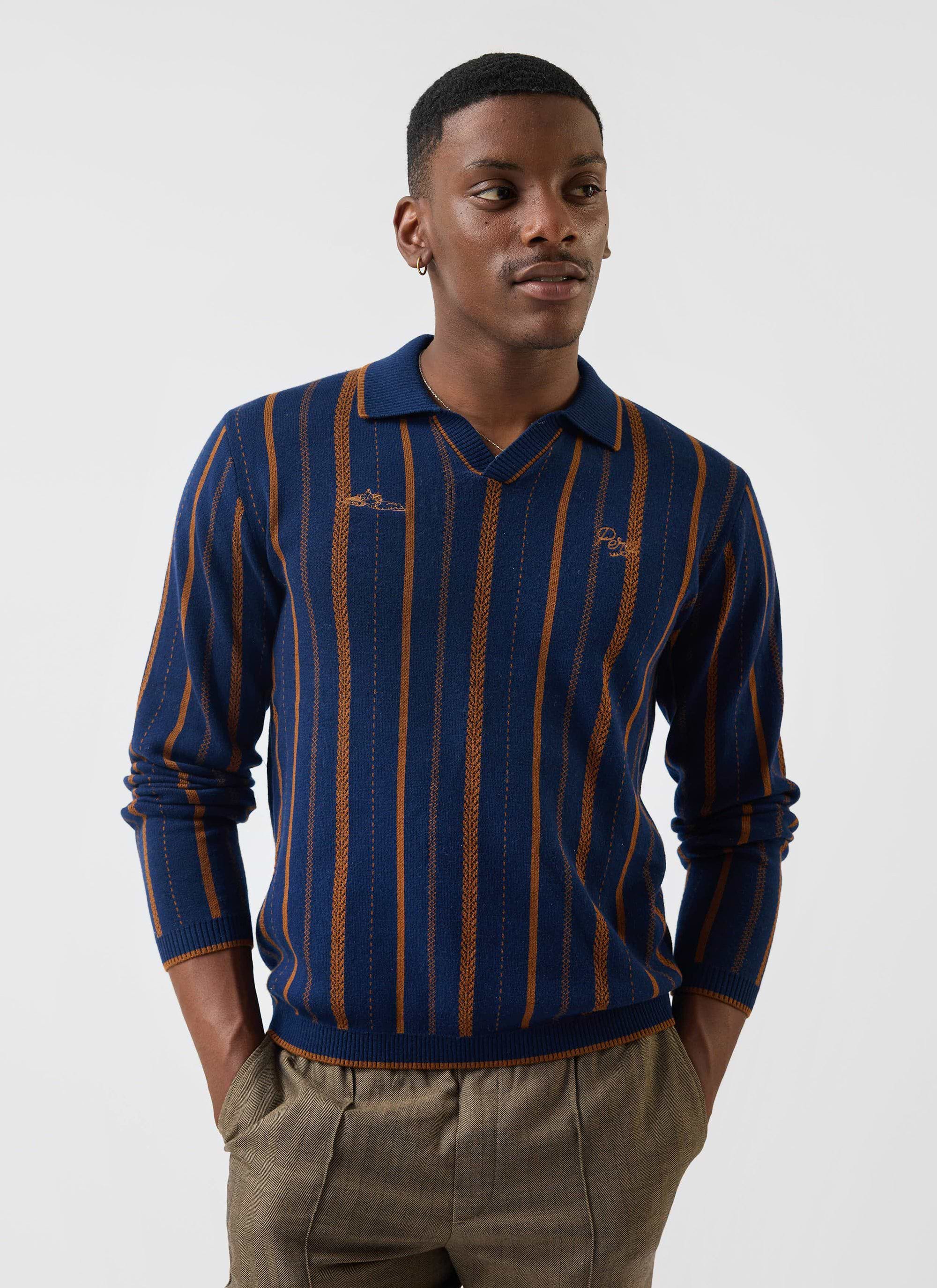 A man models the Percival Citation Knitted Football Shirt, a navy long-sleeve polo with distinctive vertical orange stripes.