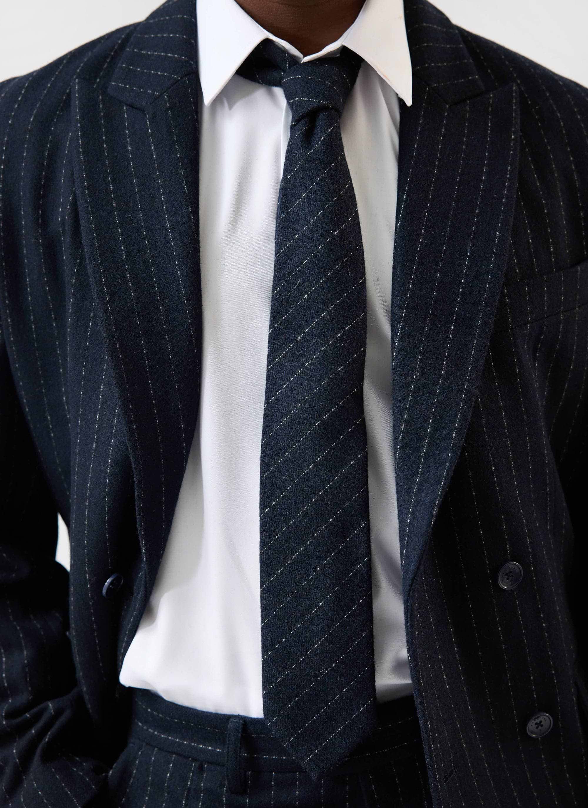 A model wears the Percival Textured Stripe Tie in navy, styled with a crisp white shirt and a matching navy pinstripe suit.
